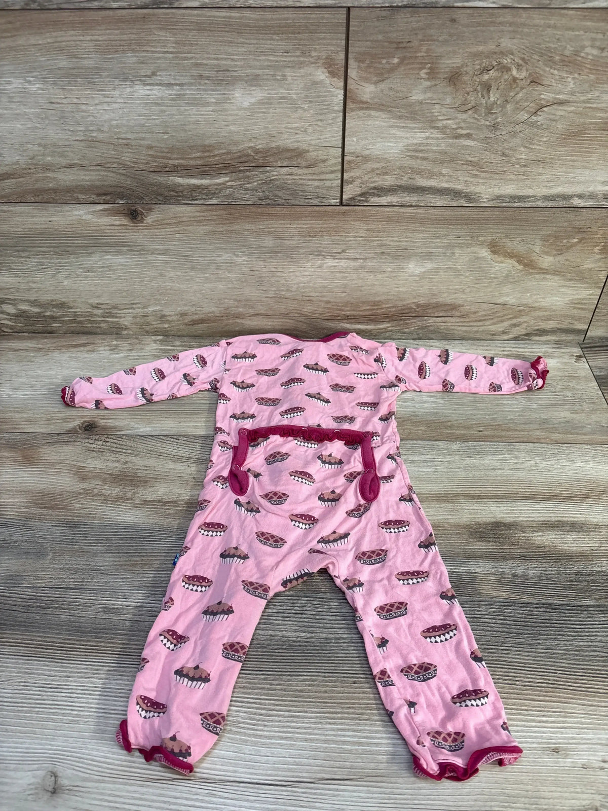 Flat-lay of pink Kickee Pants bamboo zip coverall with muffin print and ruffle trim, size 3-6 months, on wood floor