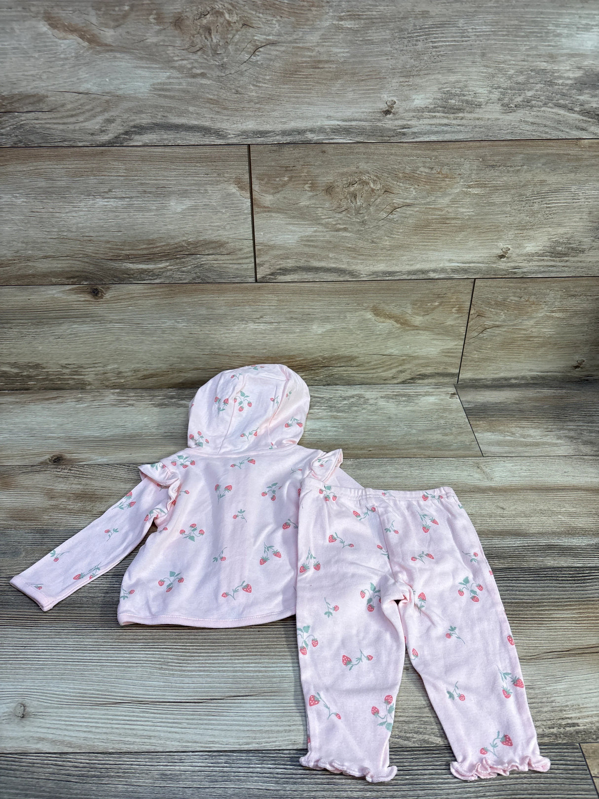 Flat lay of Child of Mine 2-piece pink hooded jacket and pants with strawberry print and ruffle hems on wood background