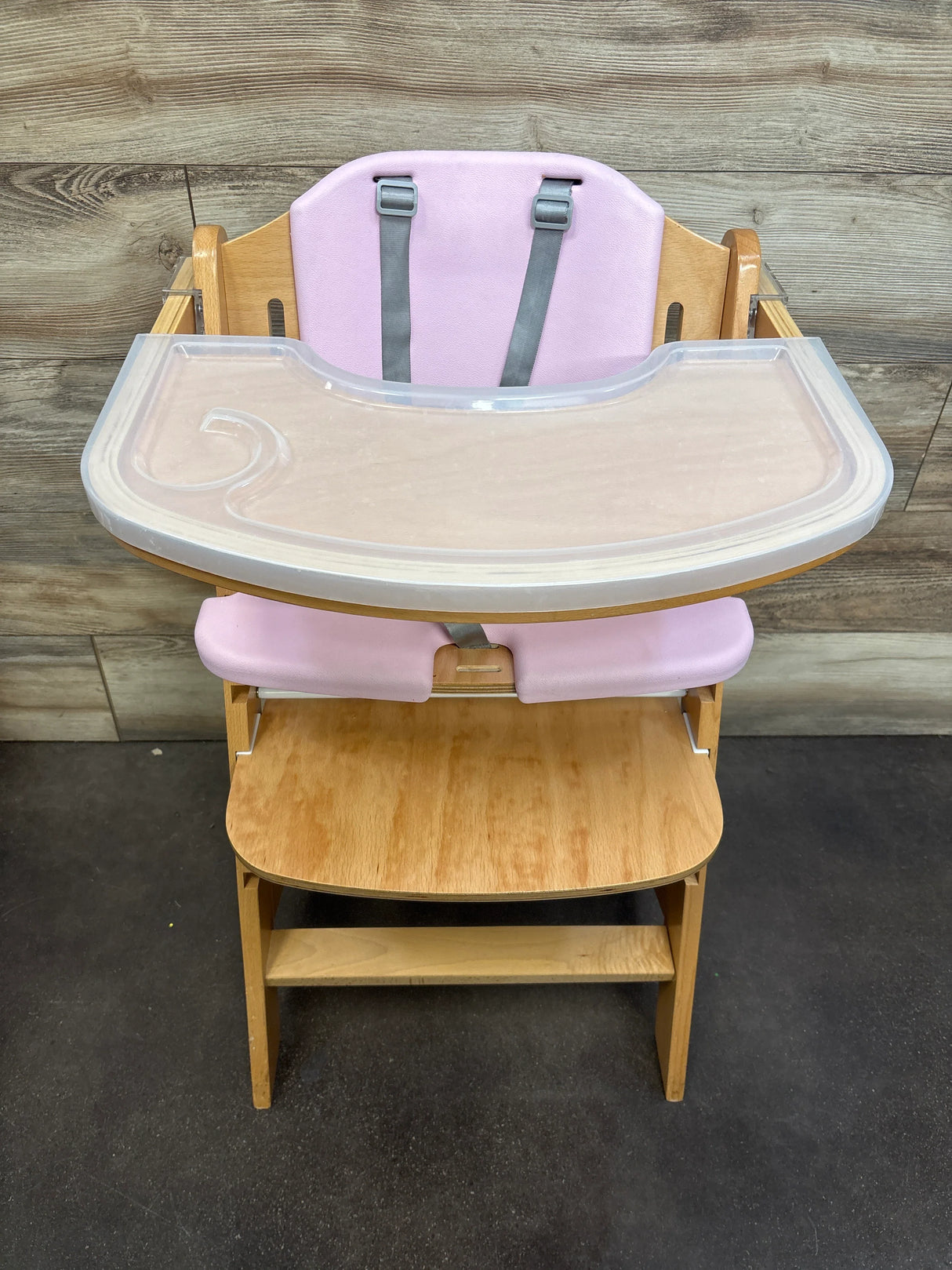 Wooden high chair with pink padding, safety straps, and clear tray for babies or toddlers