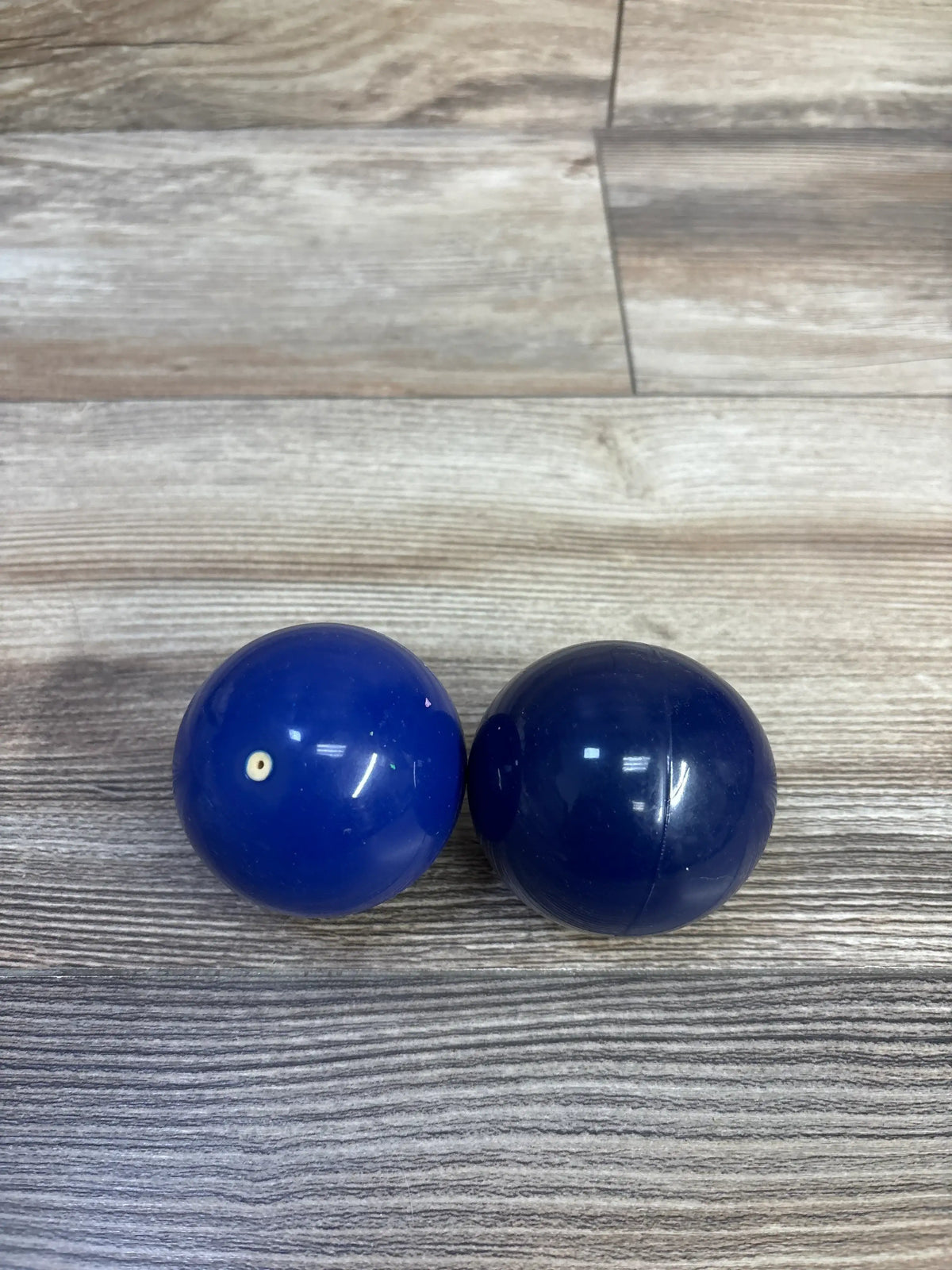 Front view of Lovevery Opposite Balls showcasing two blue balls with a wood-look floor background