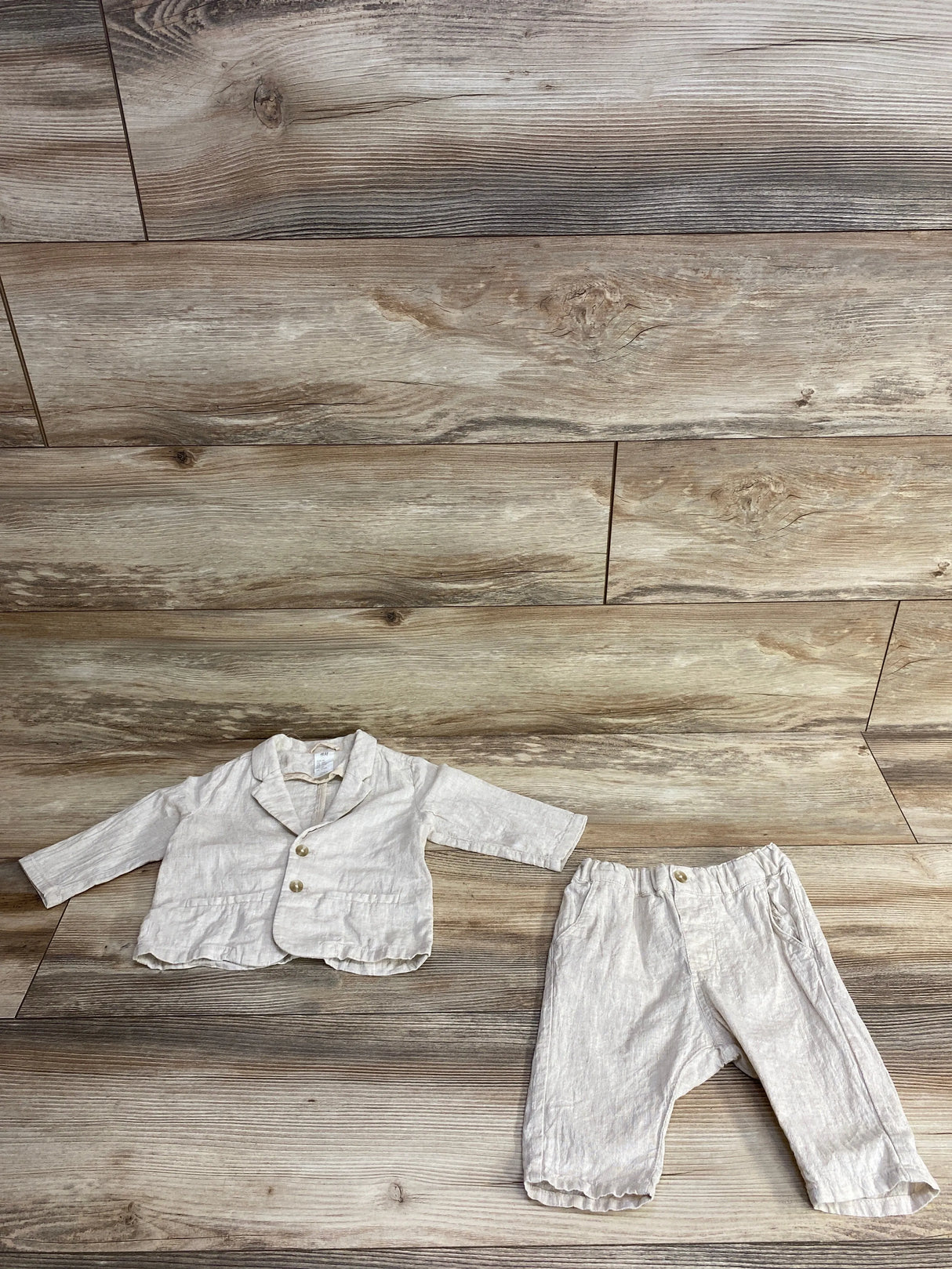 Neutral beige toddler blazer with buttons and matching pants on wood floor background