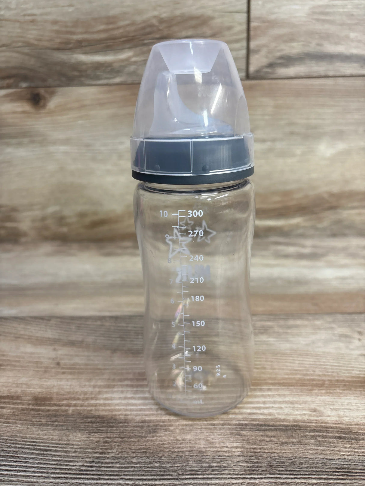 Front view of NUK Sippy Cup 10oz showing clear bottle, gray screw rim and clear cap with measurement markings on wood