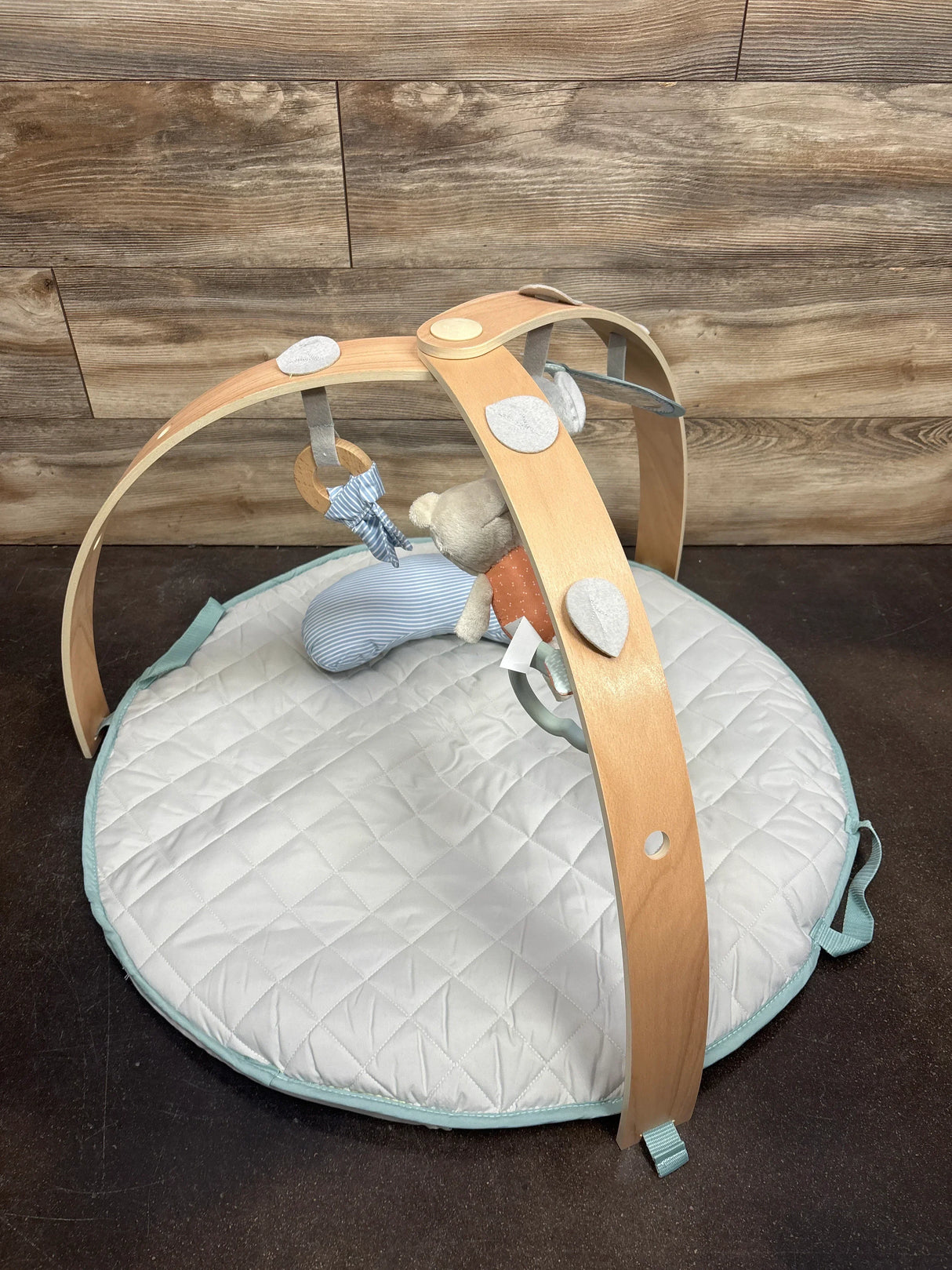 Wooden baby play gym with quilted mat and hanging plush toys on dark floor