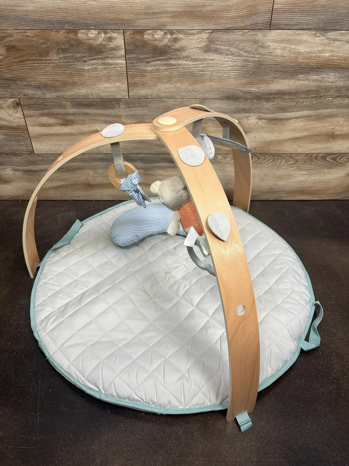 Angled view of Ingenuity Cozy Spot activity gym in Loamy with wooden arch, quilted mat with teal trim and plush toys