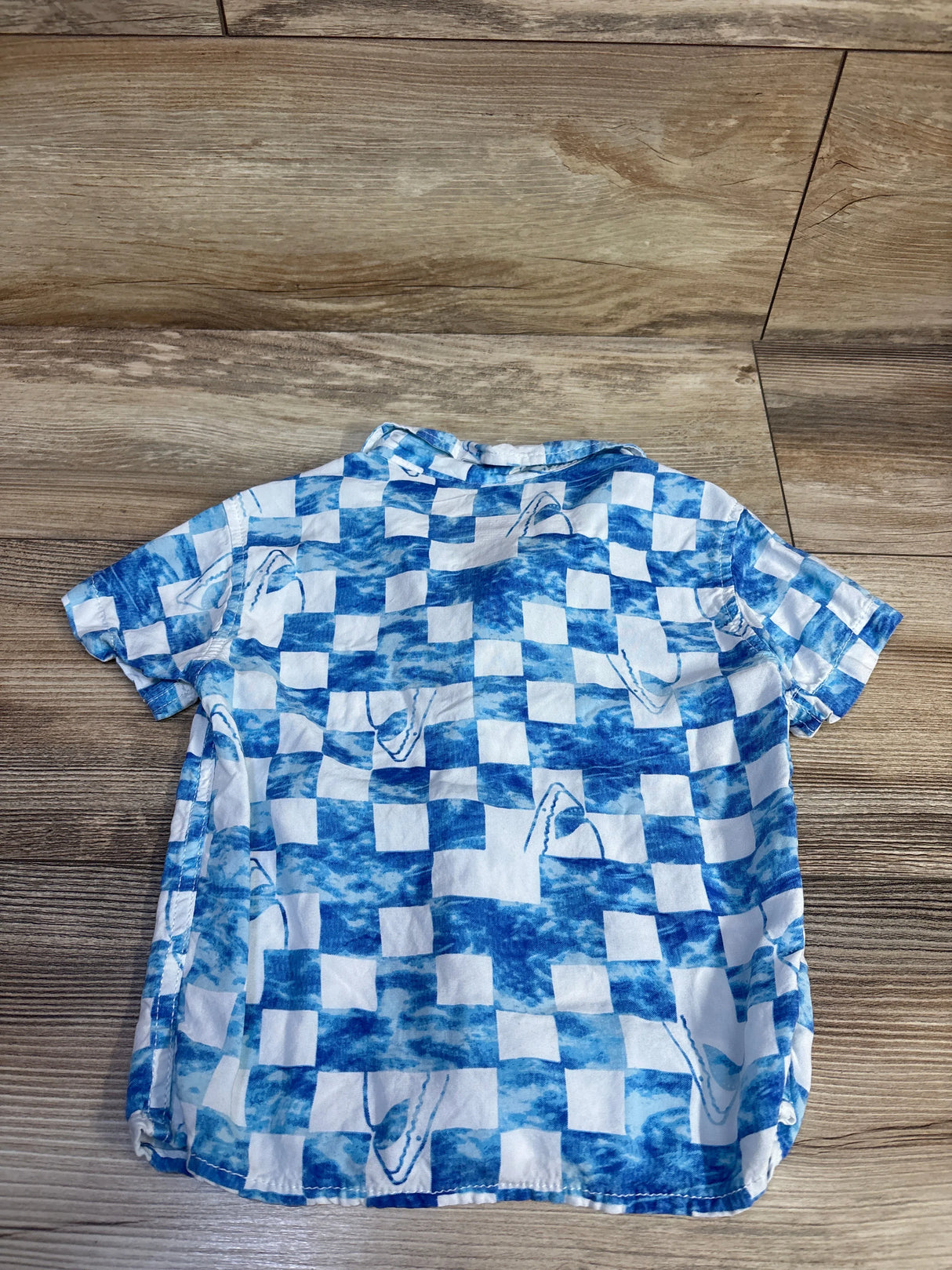 Back view of Cat & Jack short-sleeve button-up shirt showcasing blue-and-white checker print with shark fin motifs on wood floor