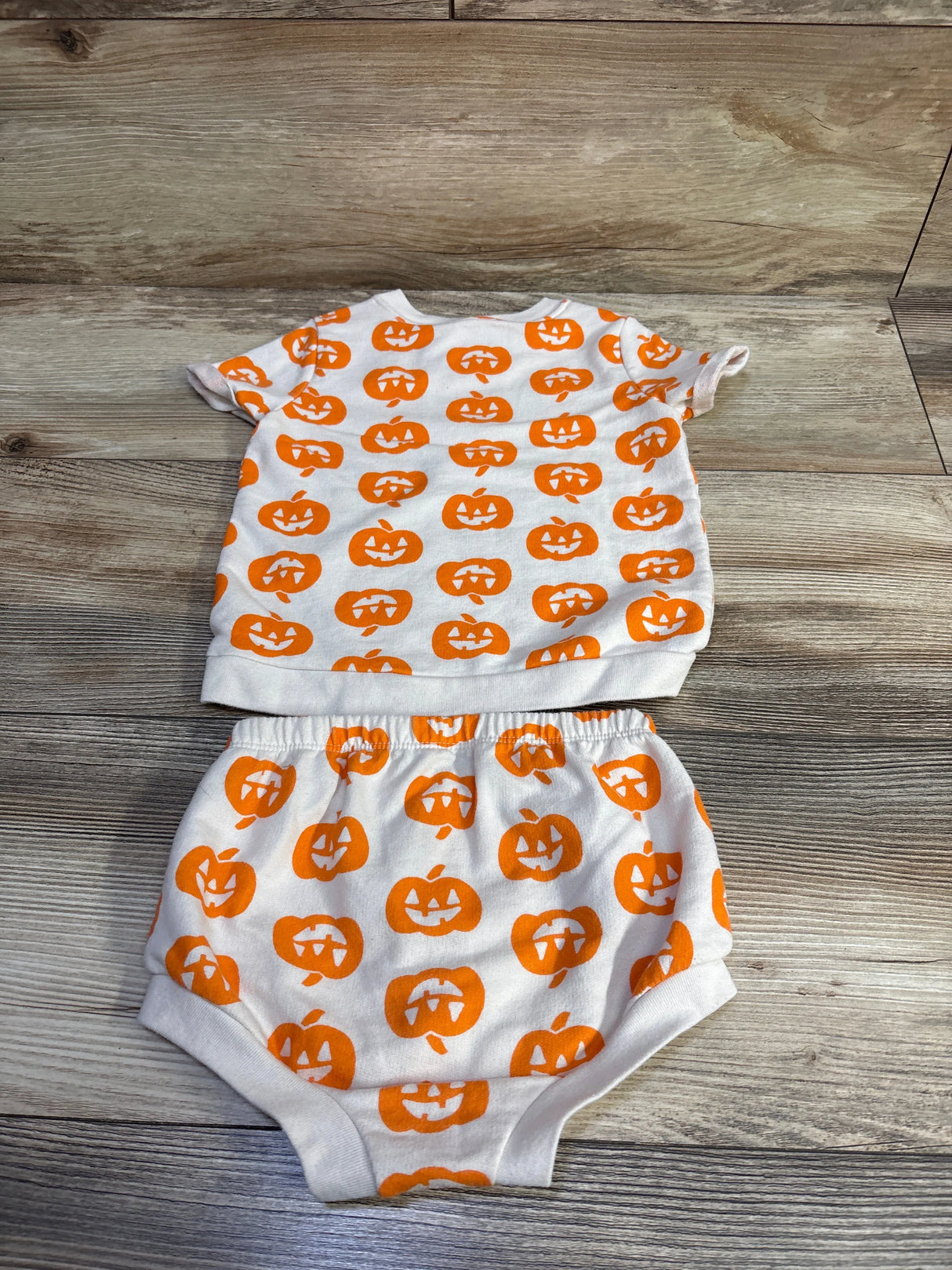 Flat lay of Cat & Jack 2-piece toddler shirt and bloomers showcasing orange jack-o-lantern print on ivory fabric with wood background