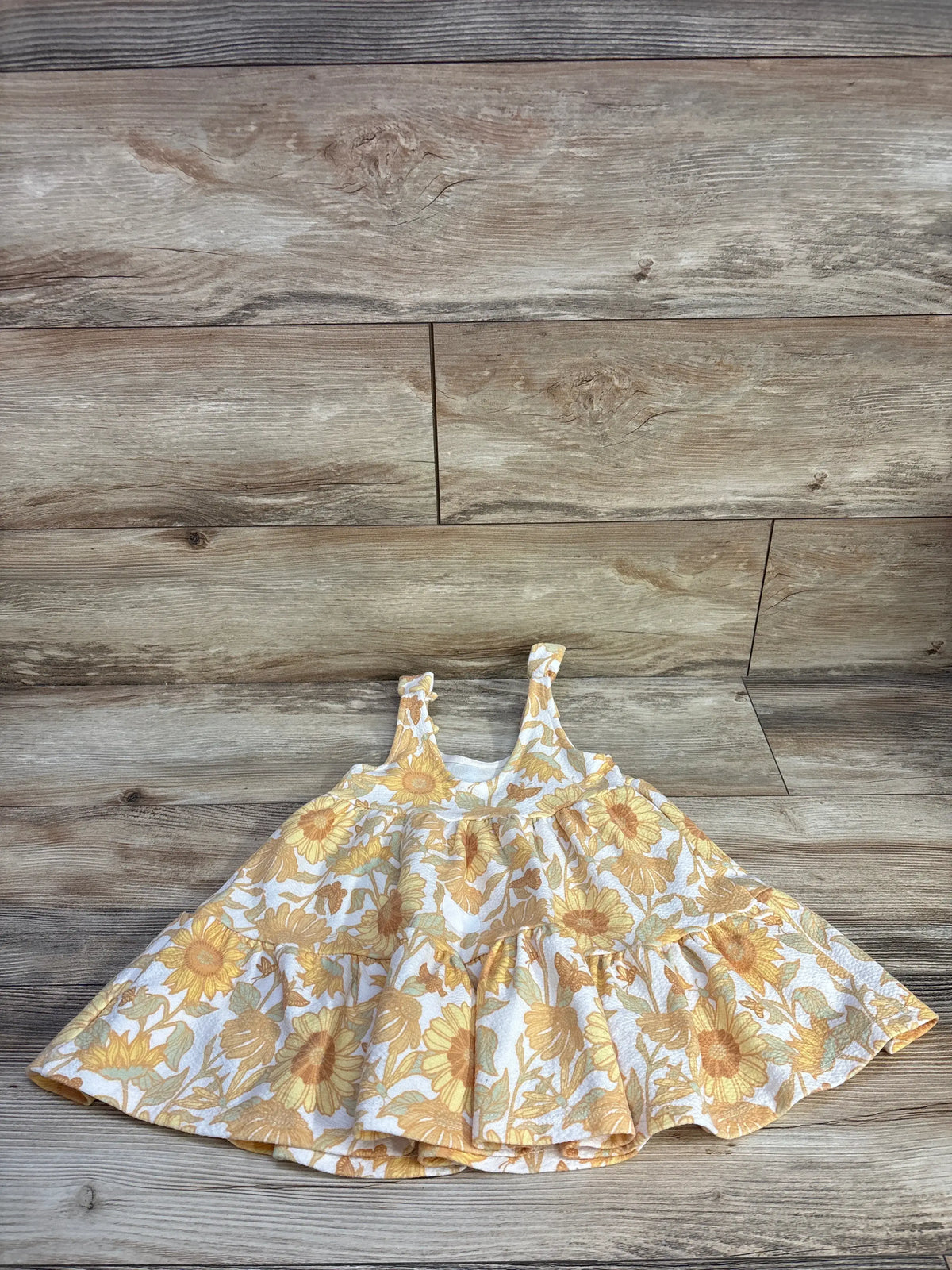 Front view of Sincerely Jules yellow floral tank dress, size 24 months, with sunflower print and flared skirt on wood planks