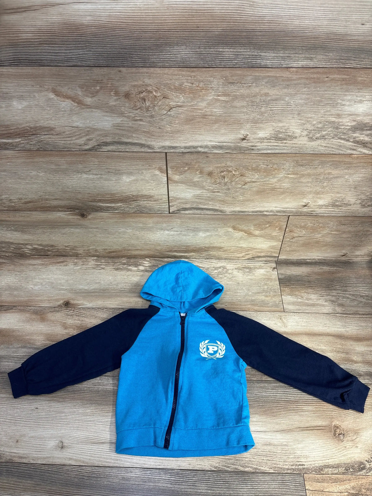 Blue and black kids zip-up hoodie with hood, emblem on chest, on wood background