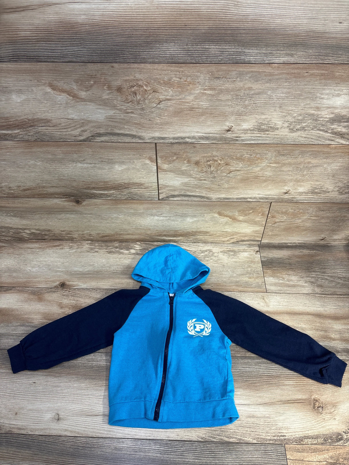 Blue and black kids zip-up hoodie with hood, emblem on chest, on wood background