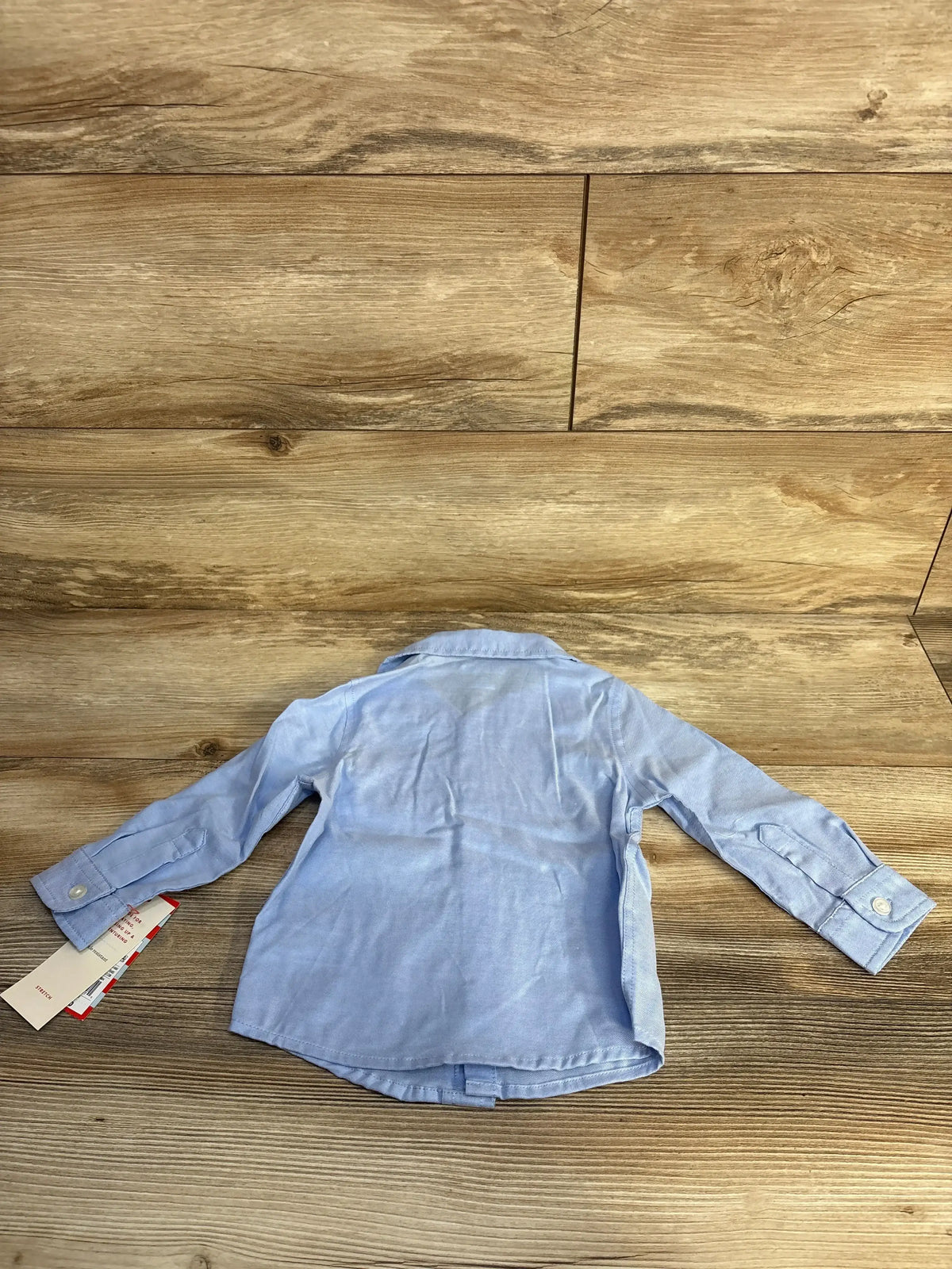 Back view of Cat & Jack blue button-up dress shirt size 12 months showing long sleeves, collar, and tags on wood floor