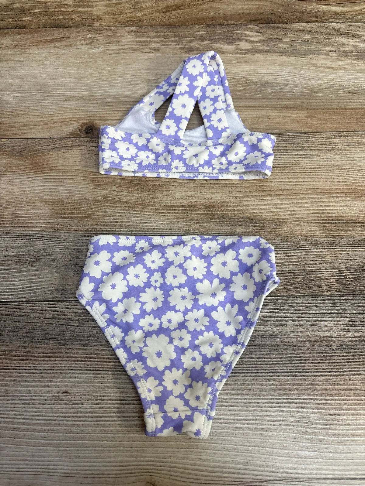 Flat lay of baby two piece purple floral swimsuit showing crisscross strap top and high rise bottoms on wood background