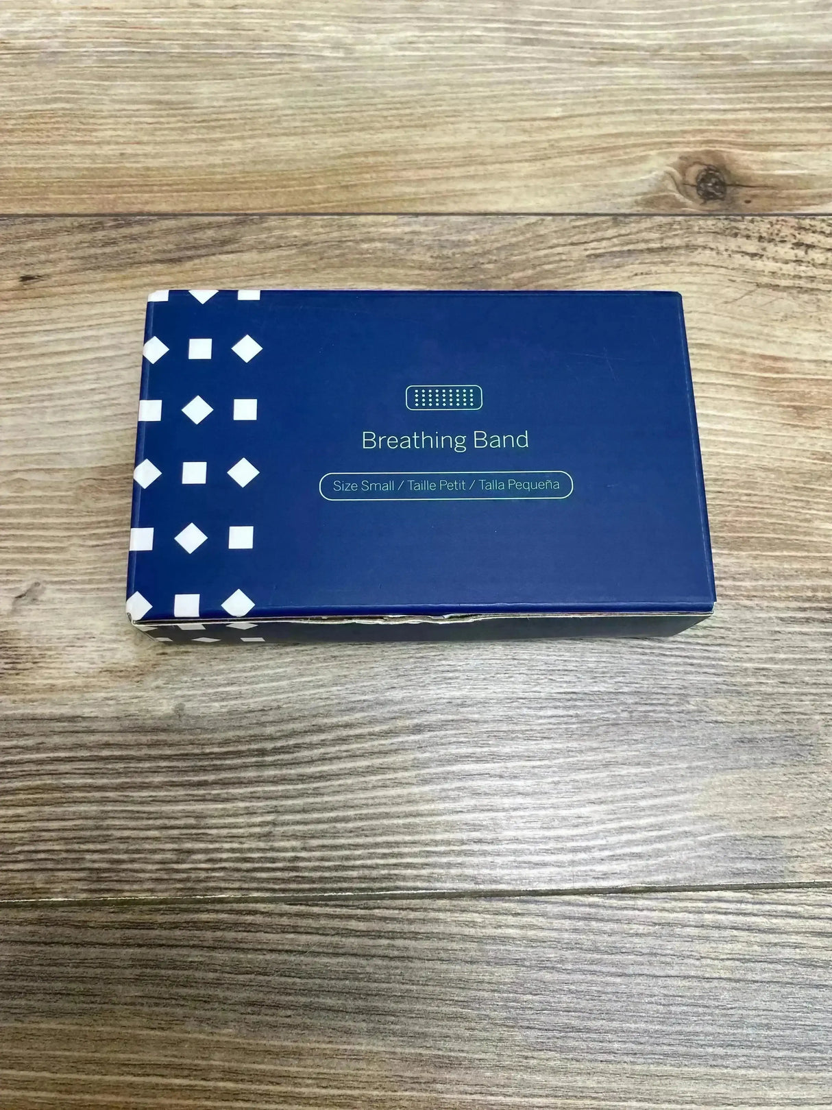 Top-down of Nanit Breathing Band box showing 'Breathing Band' label and size Small on blue packaging against wood floor