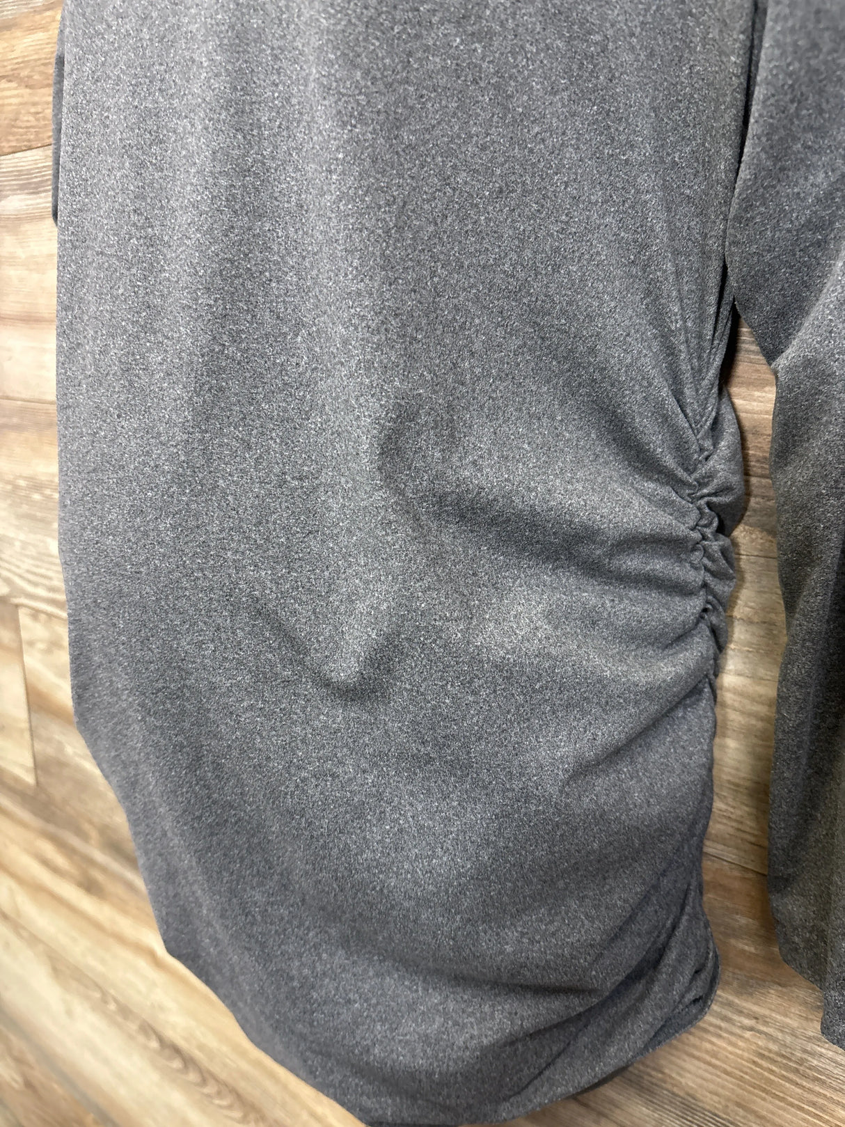 Close-up side view of Grey maternity long sleeve V-neck shirt showcasing side ruching and soft stretch fabric on a wood background
