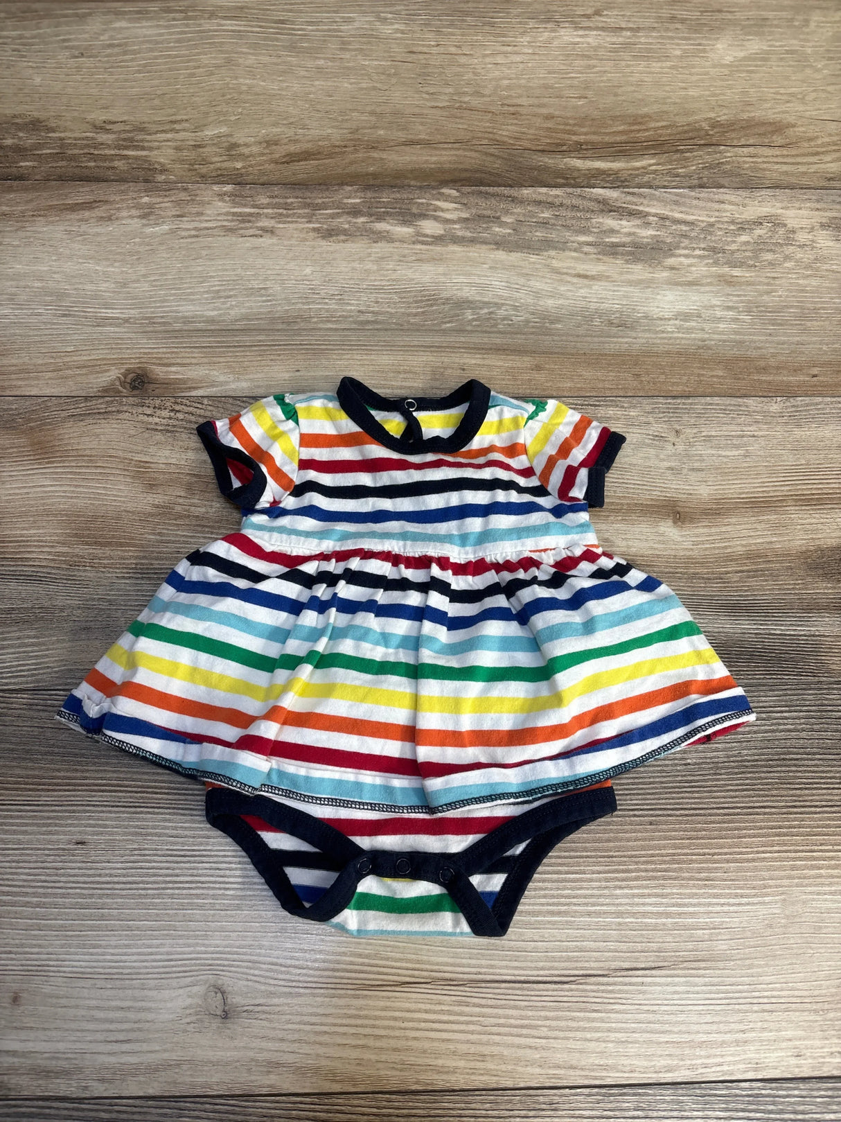 Baby dress romper with rainbow stripes and black trim on a wooden background
