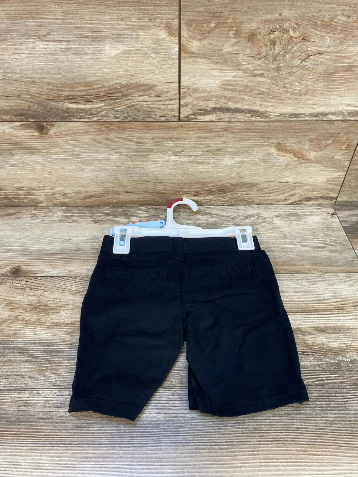 Rear view of Cat and Jack black size 4T school uniform shorts showcasing back welt pockets and belt loops on wood background