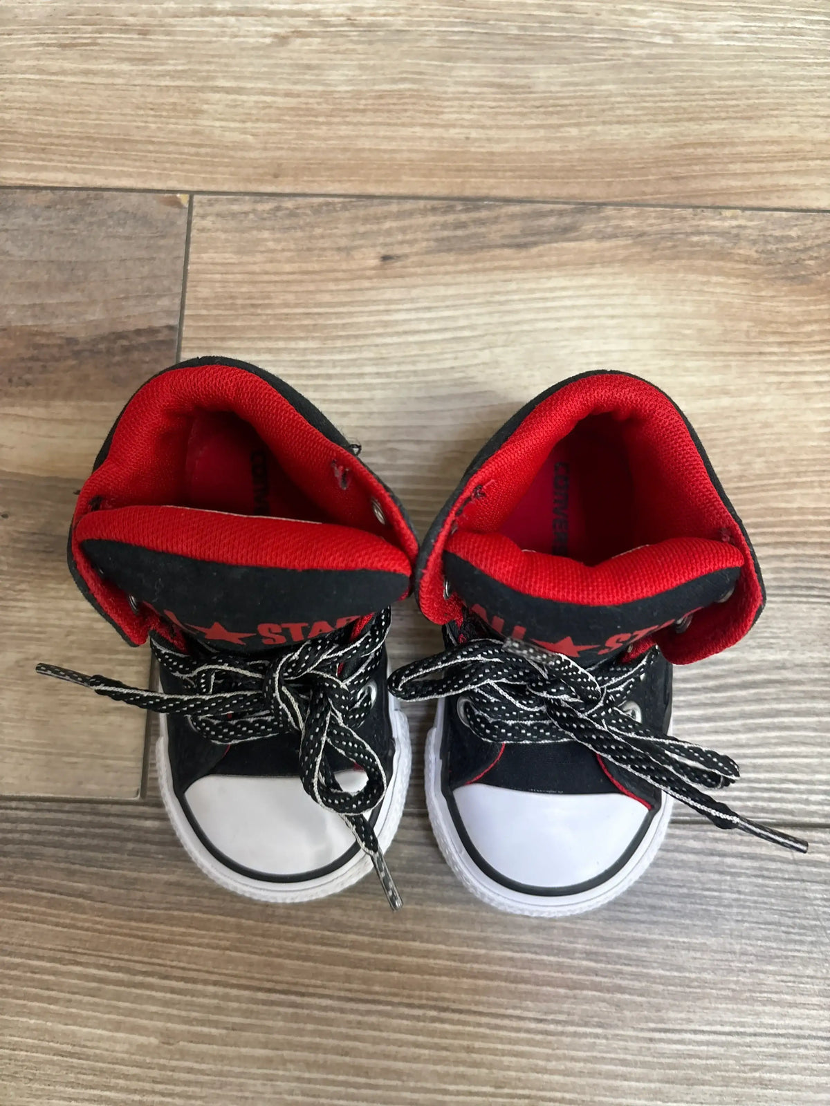 Pair of toddler-sized black and red Converse All Star sneakers with white toe caps and black-white laces on wooden floor