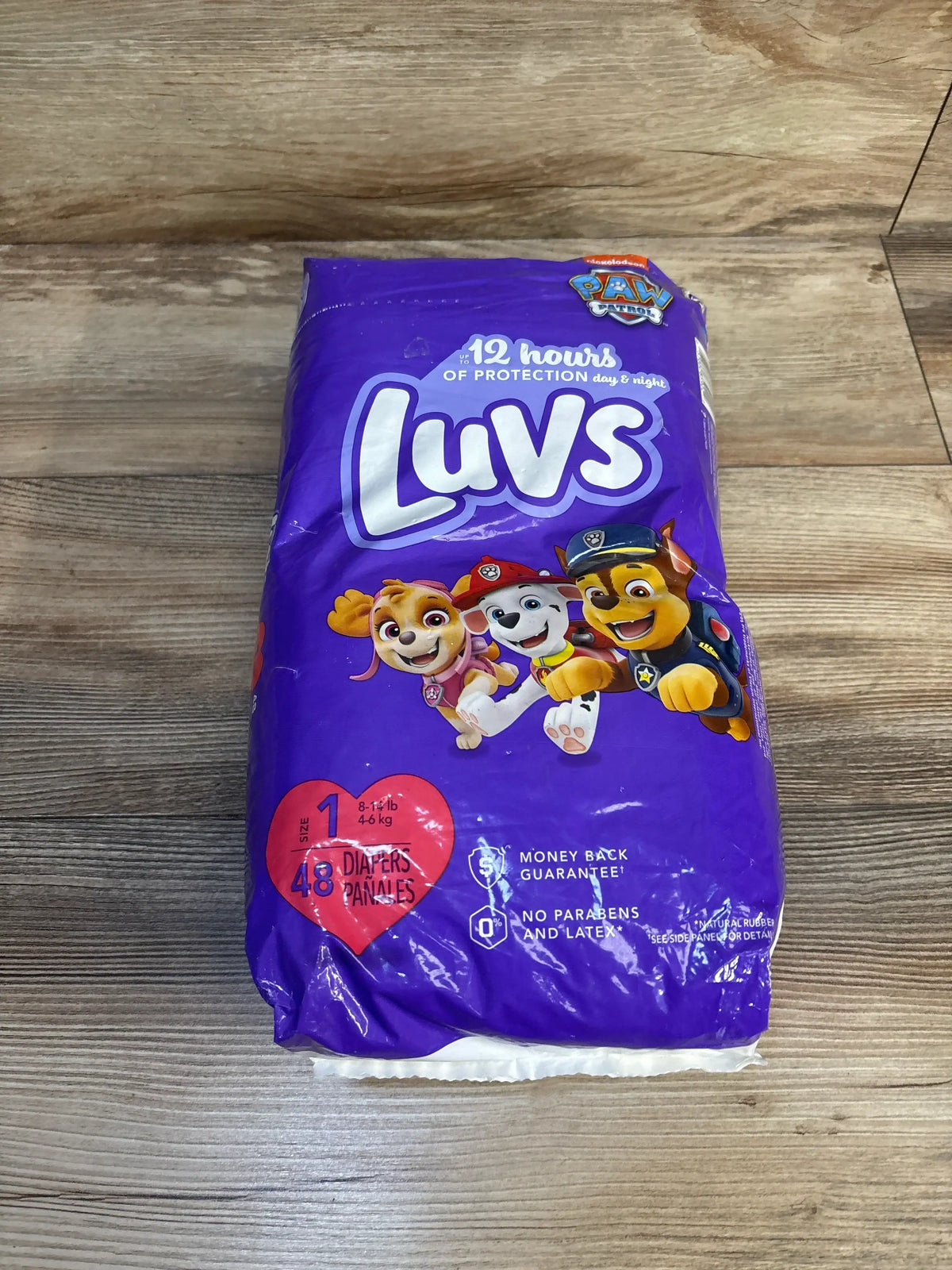 Front view of Luvs Size 1 Paw Patrol diaper pack with 48 count and 12 hours of protection label on wooden surface