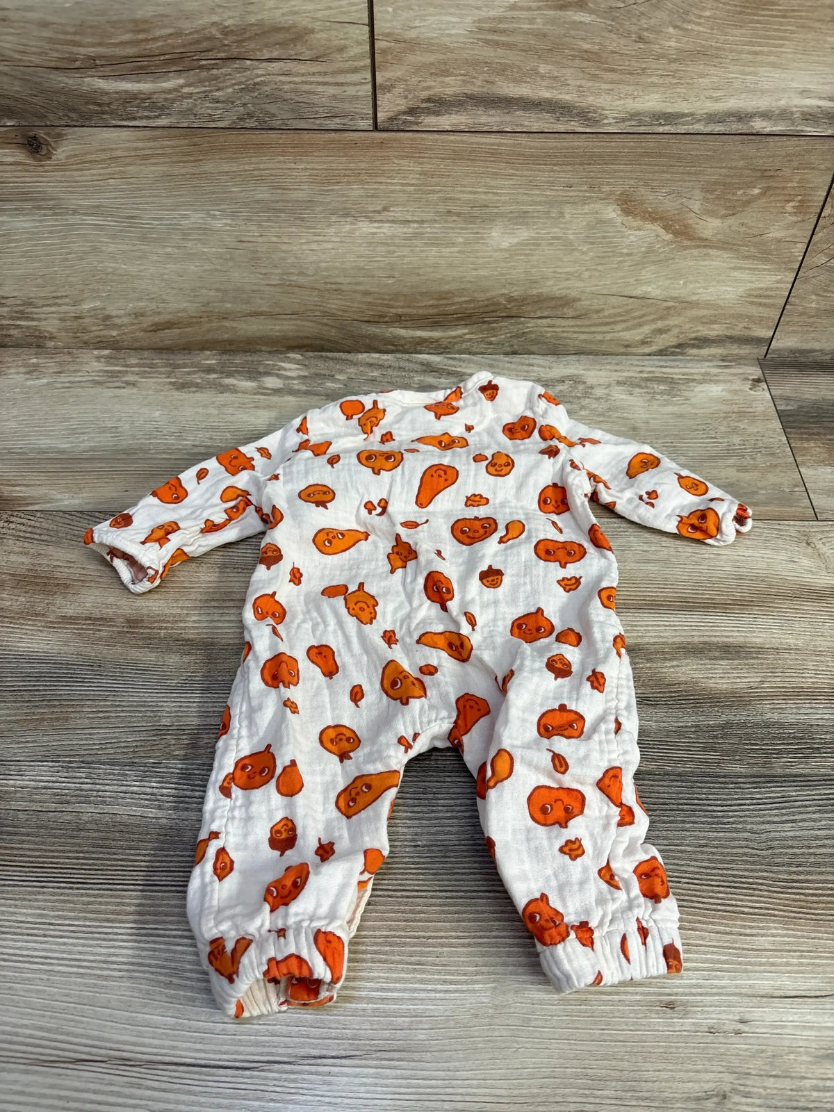 Front view of a white Cat and Jack pumpkin coverall with orange pumpkin prints on a wood look background