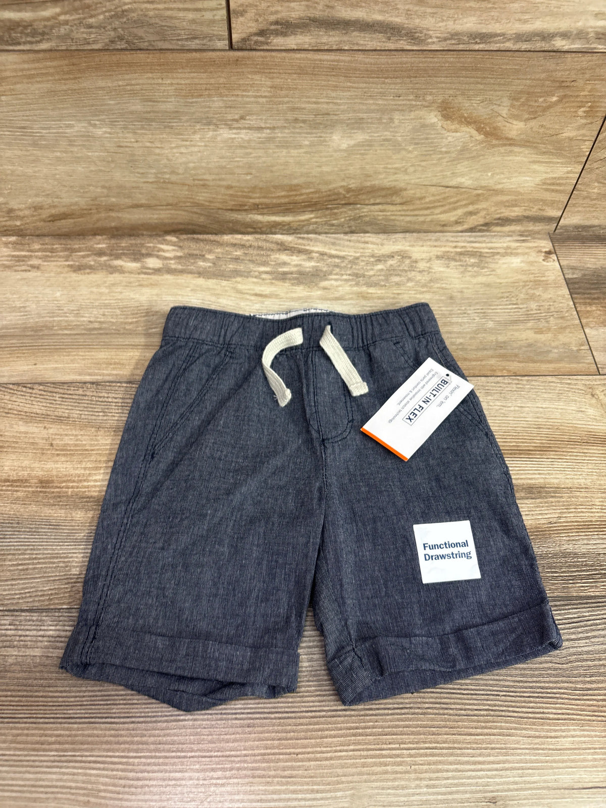 New blue chambray drawstring shorts for toddlers, size 3T, on a wood background.