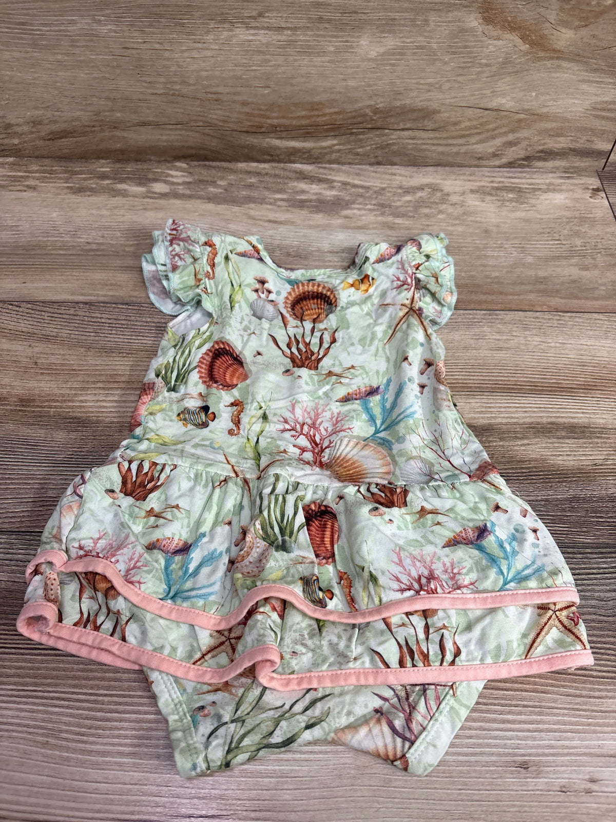 Top view of green sea animal bamboo bodysuit twirl dress showcasing flutter sleeves and pink trim on a wood surface