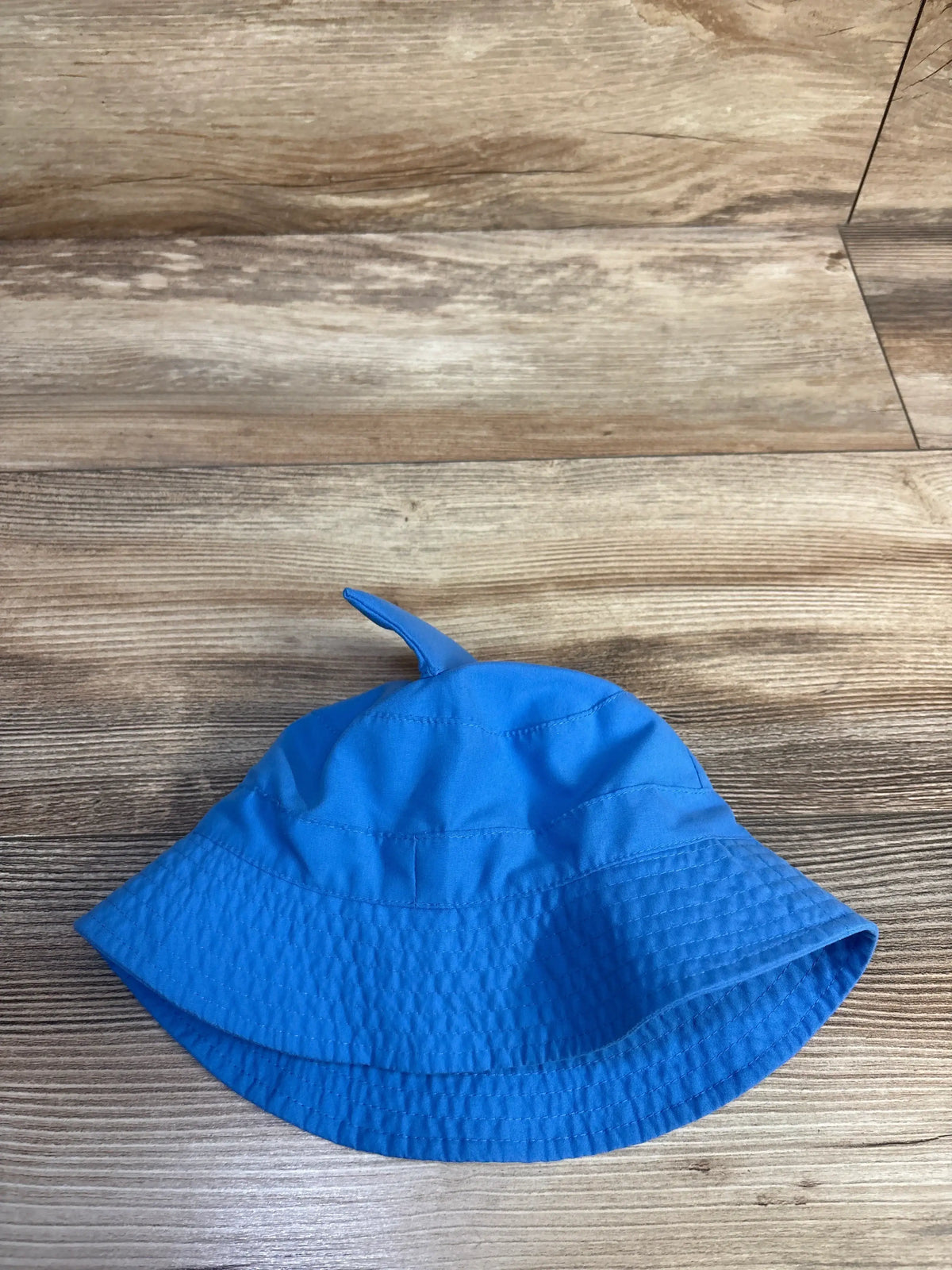 Top view of a blue shark bucket hat showcasing its shark fin design on a wood-look floor