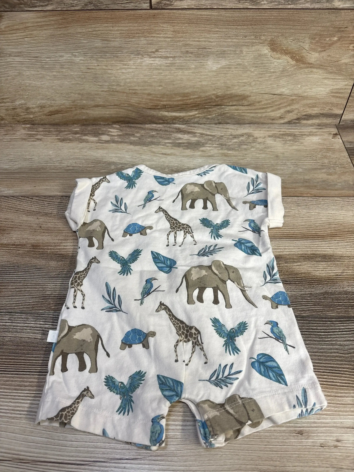 Front view of beige Little Planet organic shortie romper with safari animal print and short hemmed sleeves on wood background