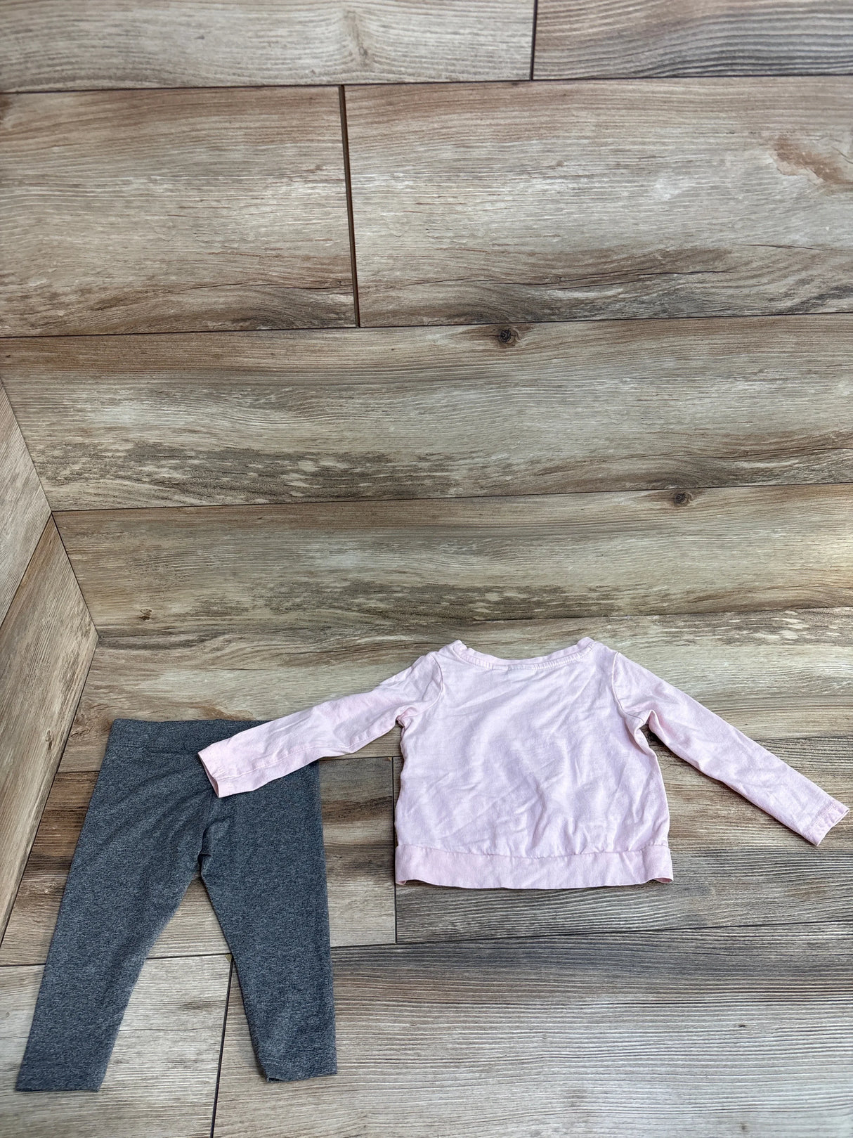 Pink long sleeve shirt and gray leggings set on wood floor background