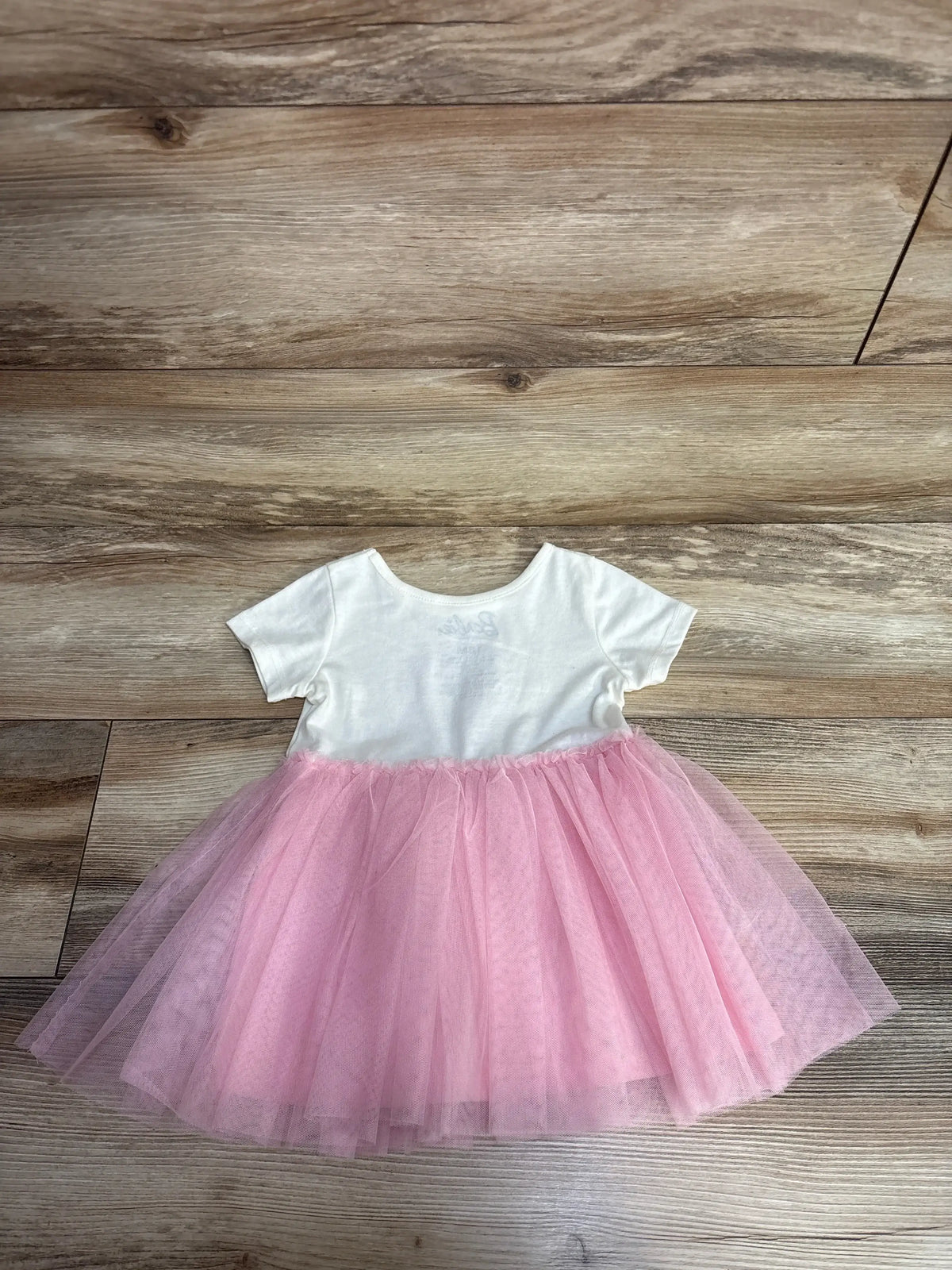 White short-sleeve baby dress with pink tulle tutu skirt on wooden floor