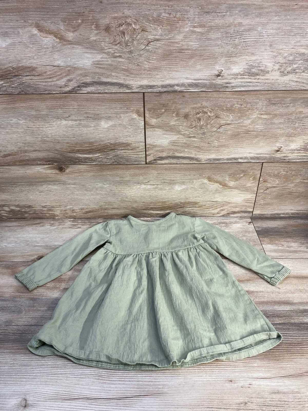 Flat lay of Cat & Jack green long-sleeve Henley dress showing gathered waist and ribbed cuffs on light wood background