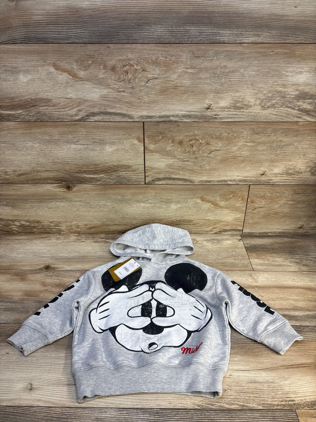 Gray kids Mickey Mouse hoodie with graphic print, laid on wood floor, great for toddler clothing resale