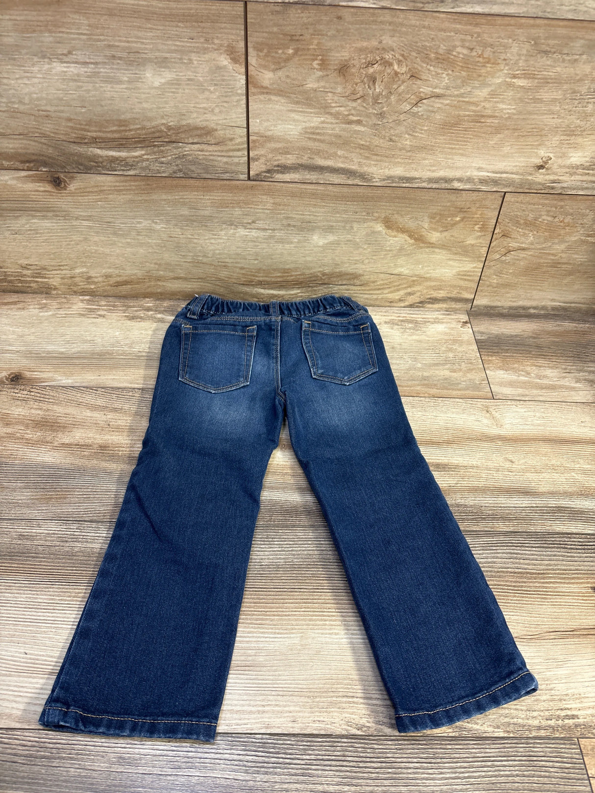 Back view of Old Navy toddler straight-leg blue jeans showcasing elastic waistband and two back pockets on wood floor background