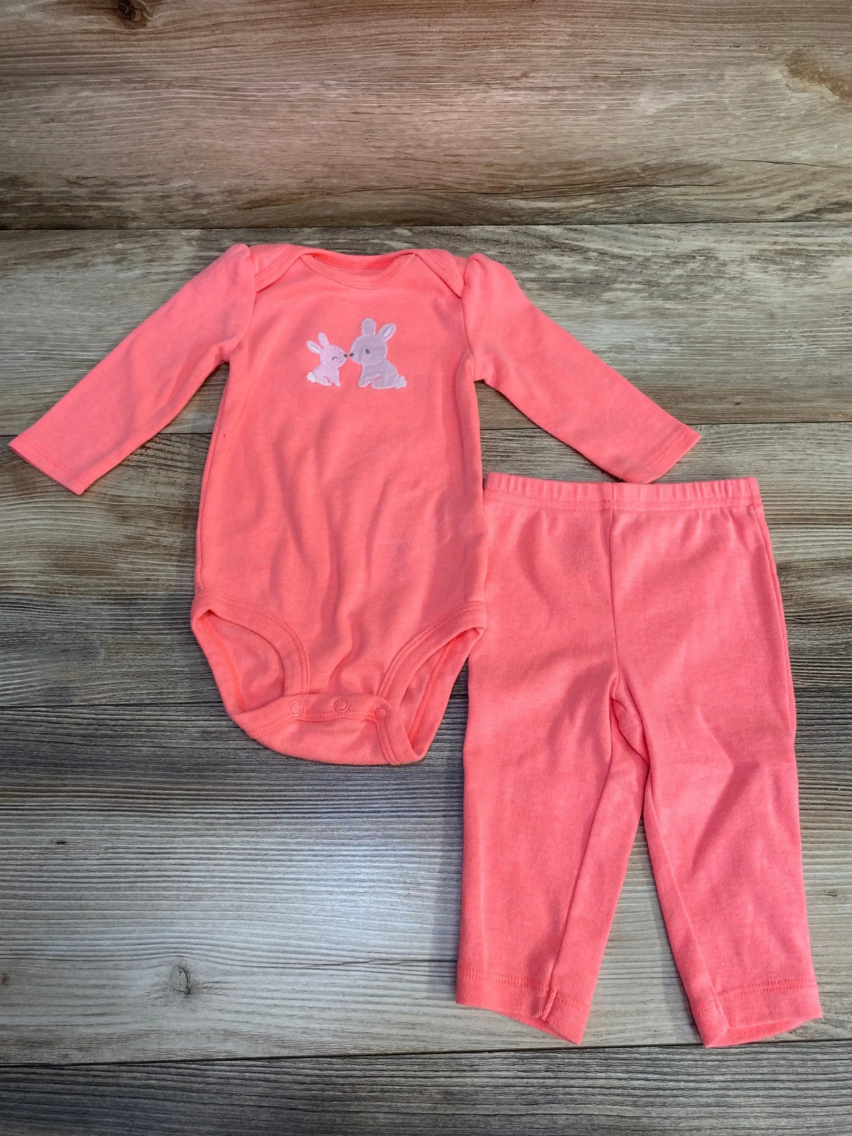 Top view of Simple Joys pink 2-piece bodysuit and pants showing embroidered bunny, snap crotch and elastic waist on wood