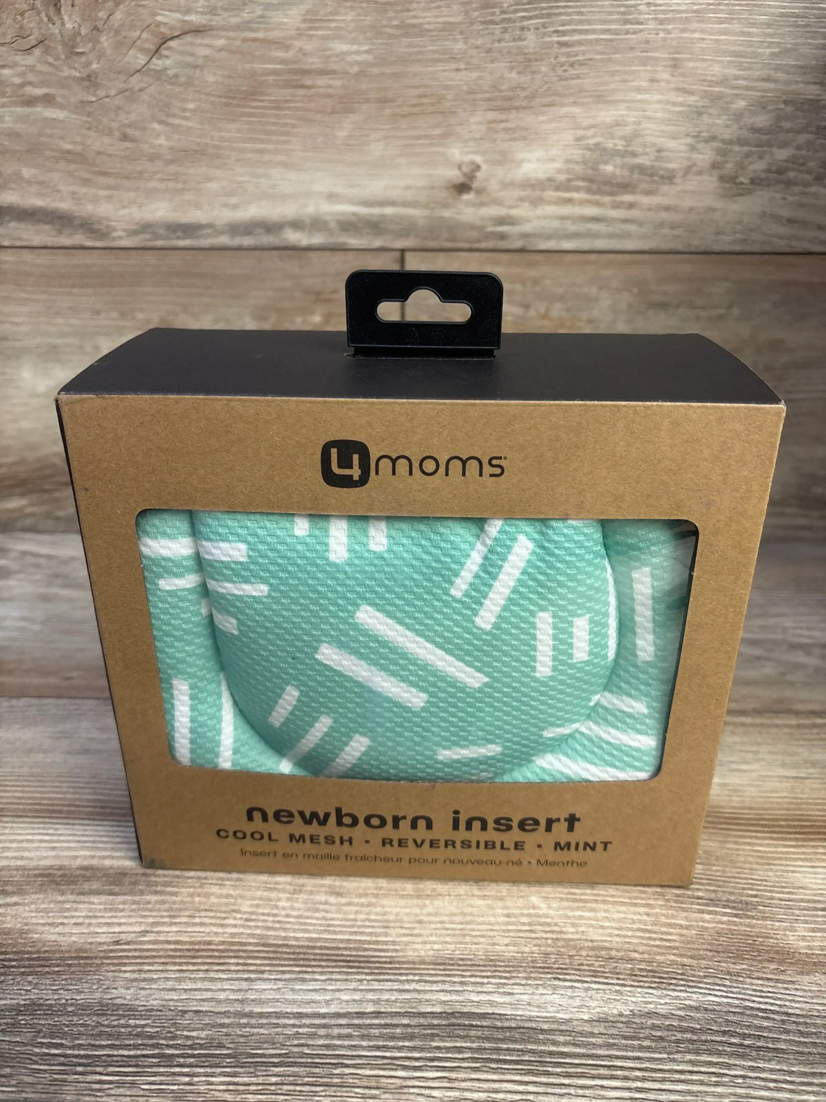 Front view of 4Moms Cool Mesh Newborn Insert in mint packaging, showcasing the patterned reversible insert on a wood surface