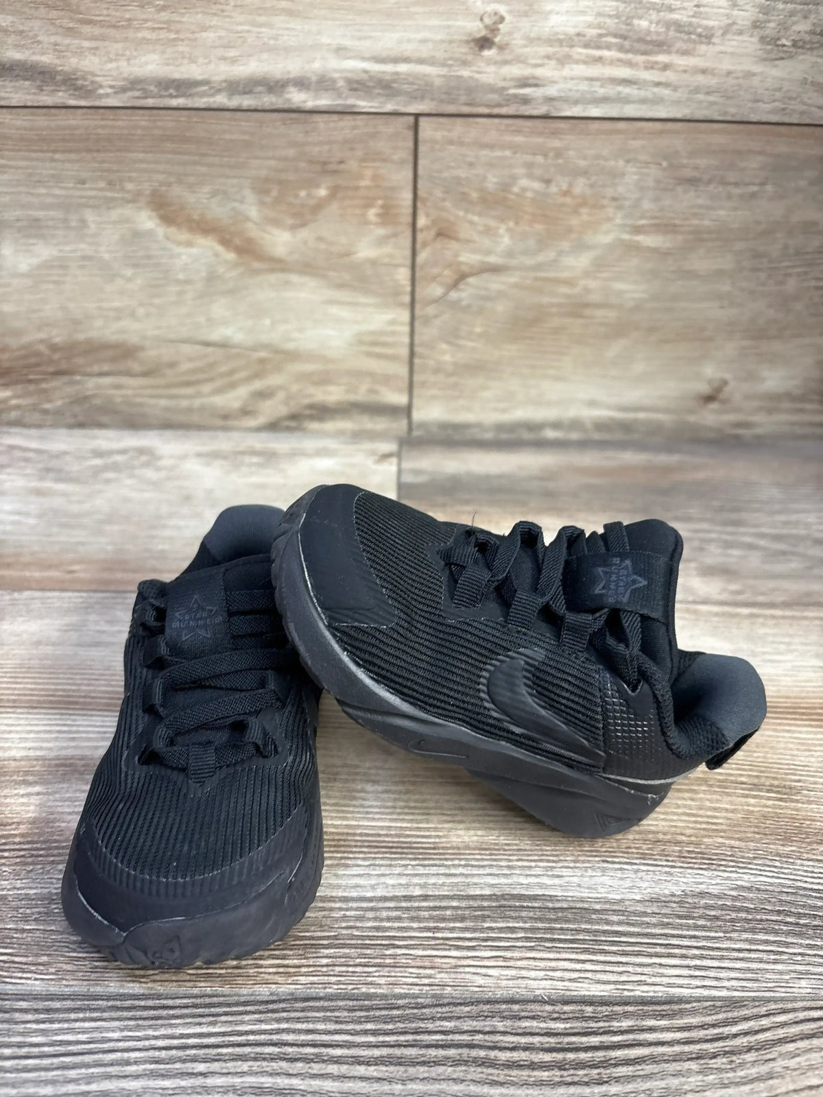 Three-quarter view of Nike Star Runner 4 toddler sneakers showing triple-black knit upper and molded sole on wood floor
