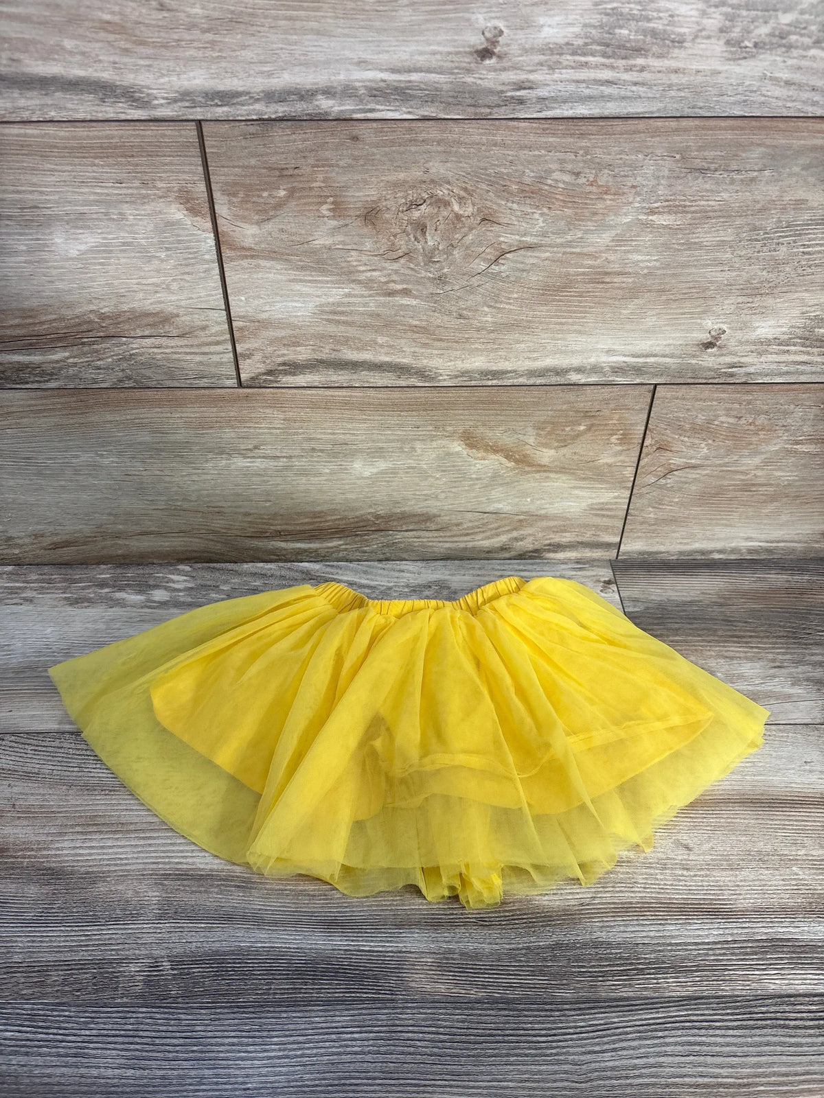 Front view of yellow Shein tulle skirt for toddlers, showcasing layered tulle and elastic waistband on a wood-look floor