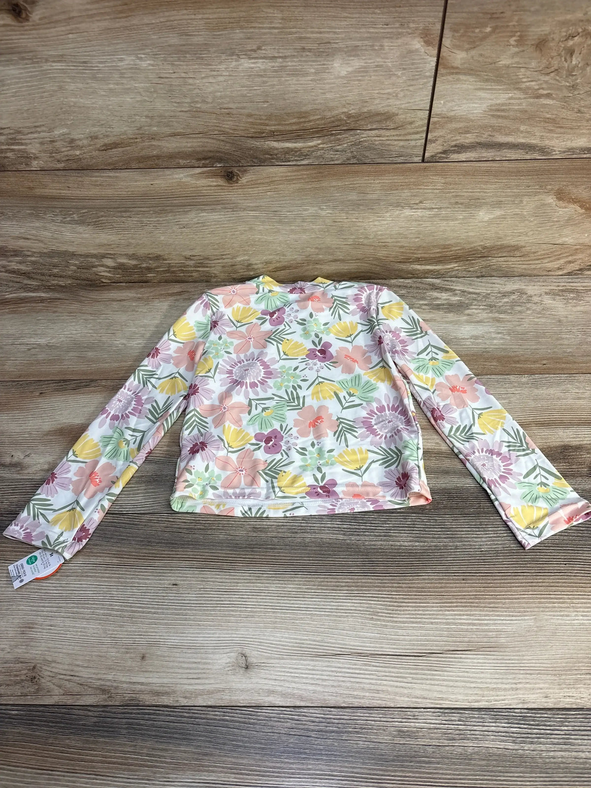 Flat lay of toddler long-sleeve white floral rashguard (5T) showing full back and sleeves on wood background