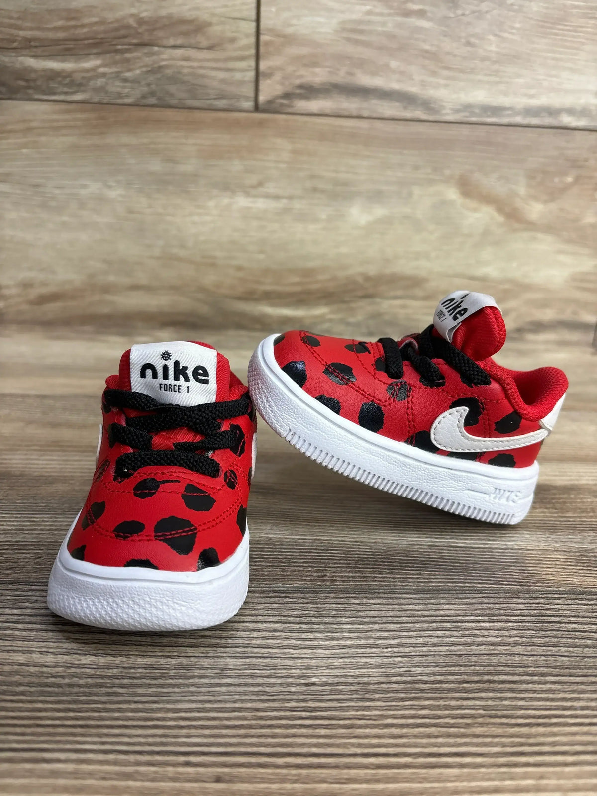 Red and black spotted Nike Force 1 toddler shoes with white soles on wooden surface
