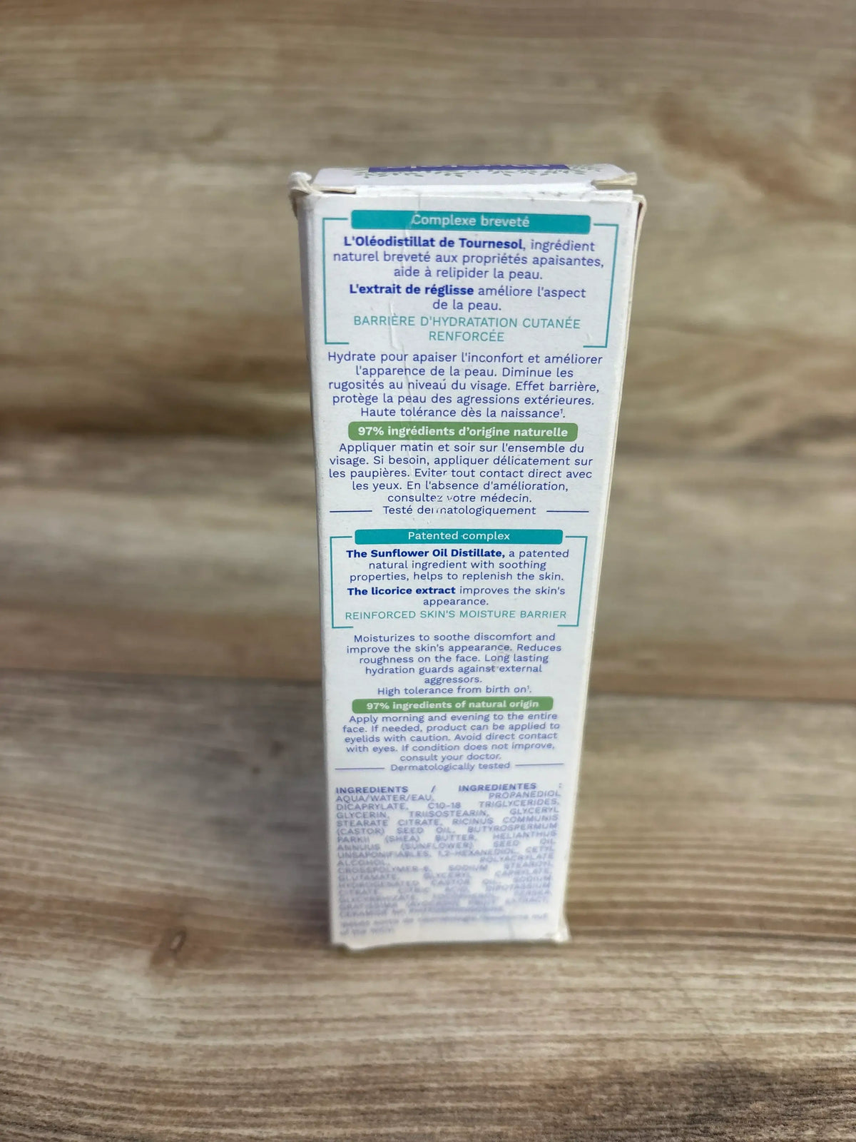 Back view of Mustela Stelatopia baby face cream box showing ingredient list and 97% natural origin text on wooden tabletop