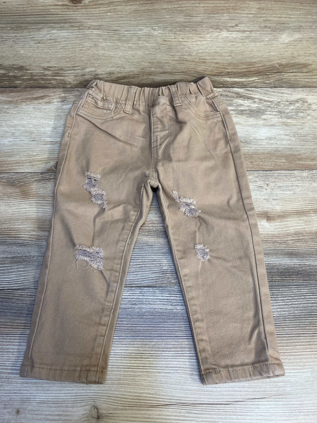 Light brown distressed kids pants with elastic waistband on wood floor