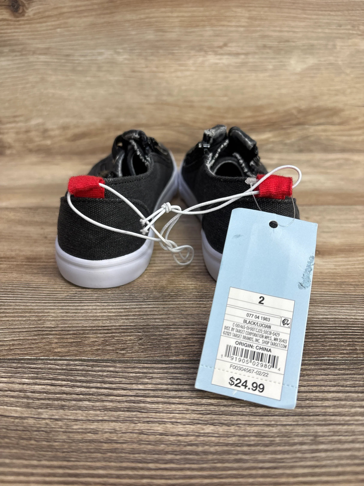 Pair of black toddler shoes with white soles and red heel tabs on wooden floor with $24.99 price tag