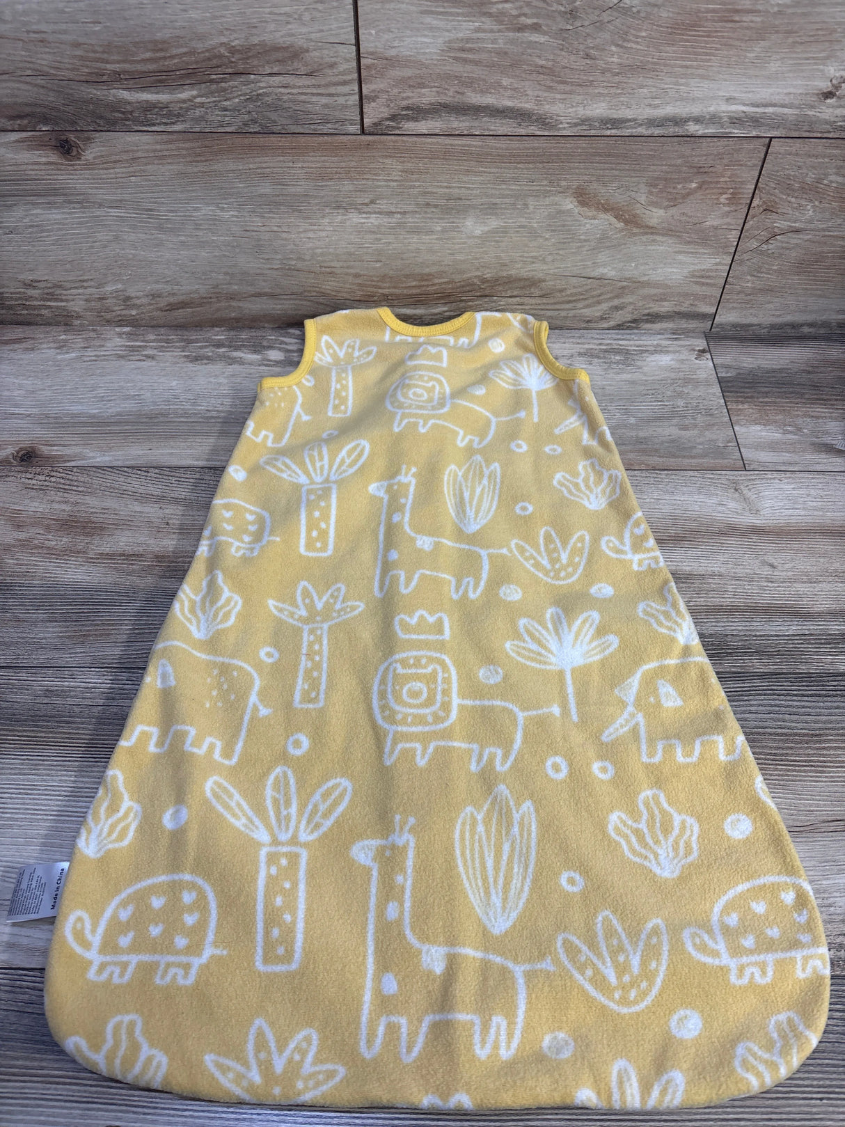 Front view of yellow blanket sleep sack for 0 to 6 months showcasing white animal pattern on wood-look flooring