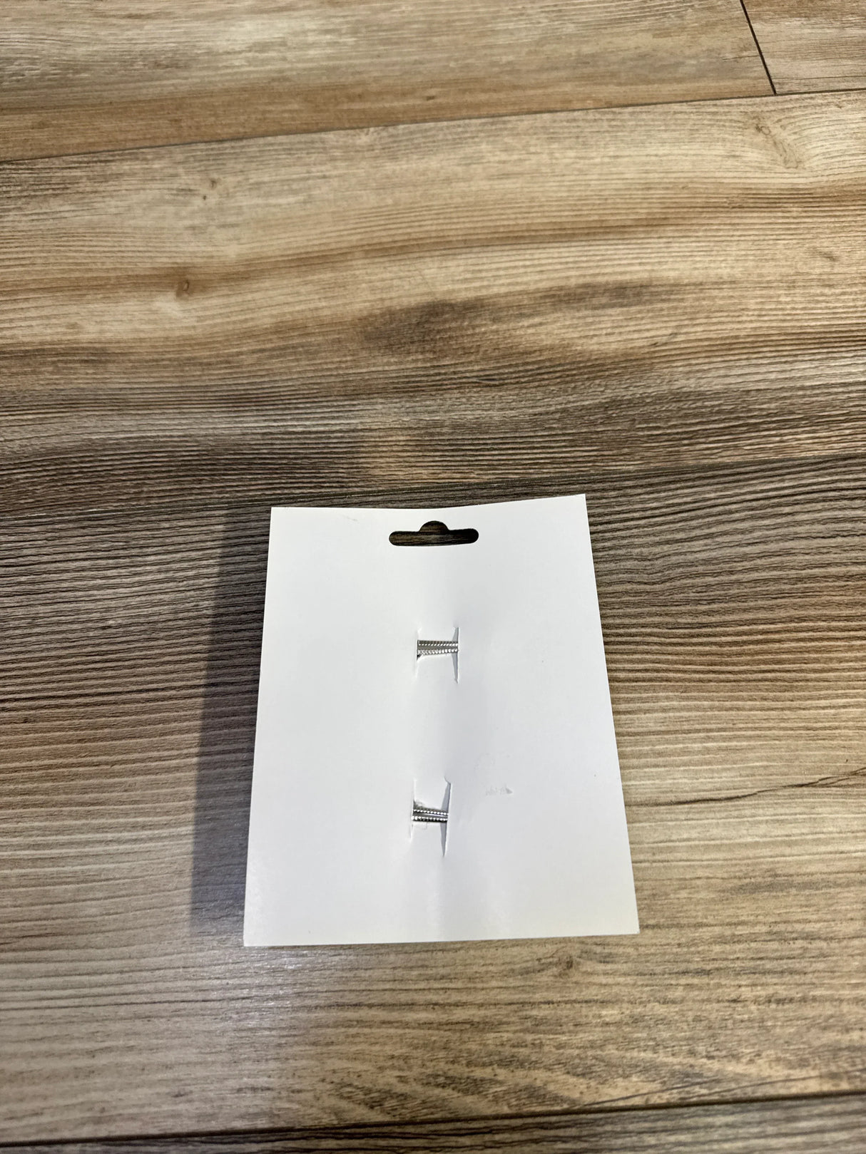 Silver kids' bar earrings on white card, wood floor background
