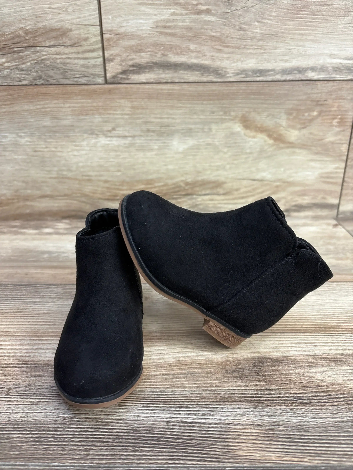 Pair of black suede toddler ankle boots with side zippers on wood background