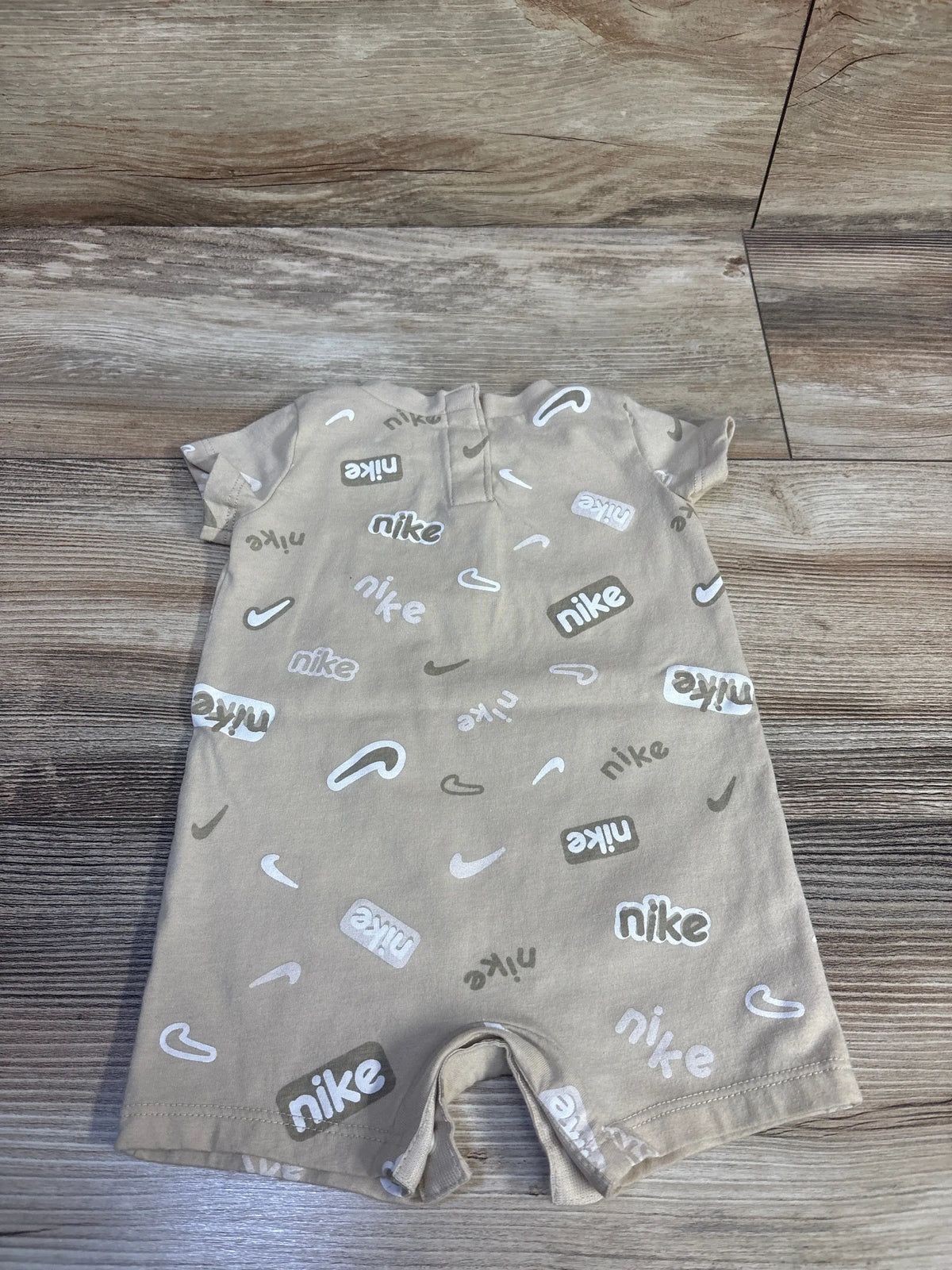 Beige baby romper with white Me n Mommy To Be logo print on a wood surface.