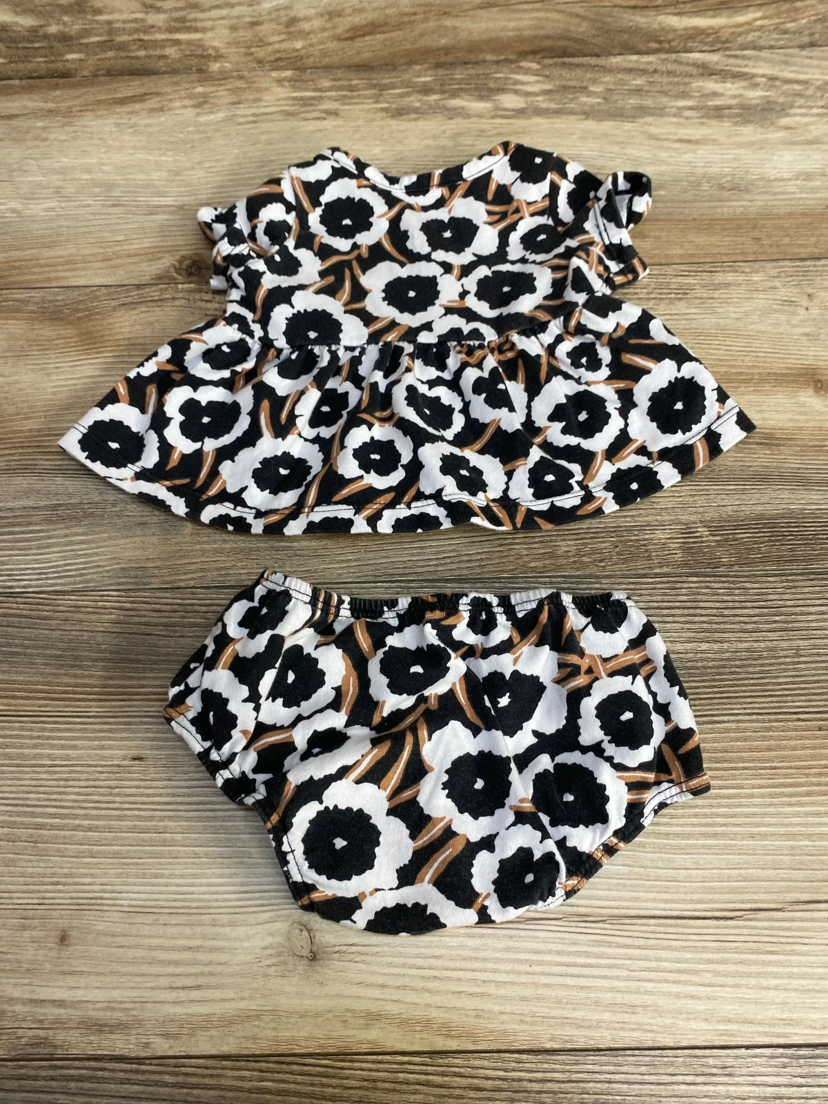 Flat lay of Diane Von Furstenberg baby faux wrap top and bloomers showing black and white floral print with brown accents on wood background
