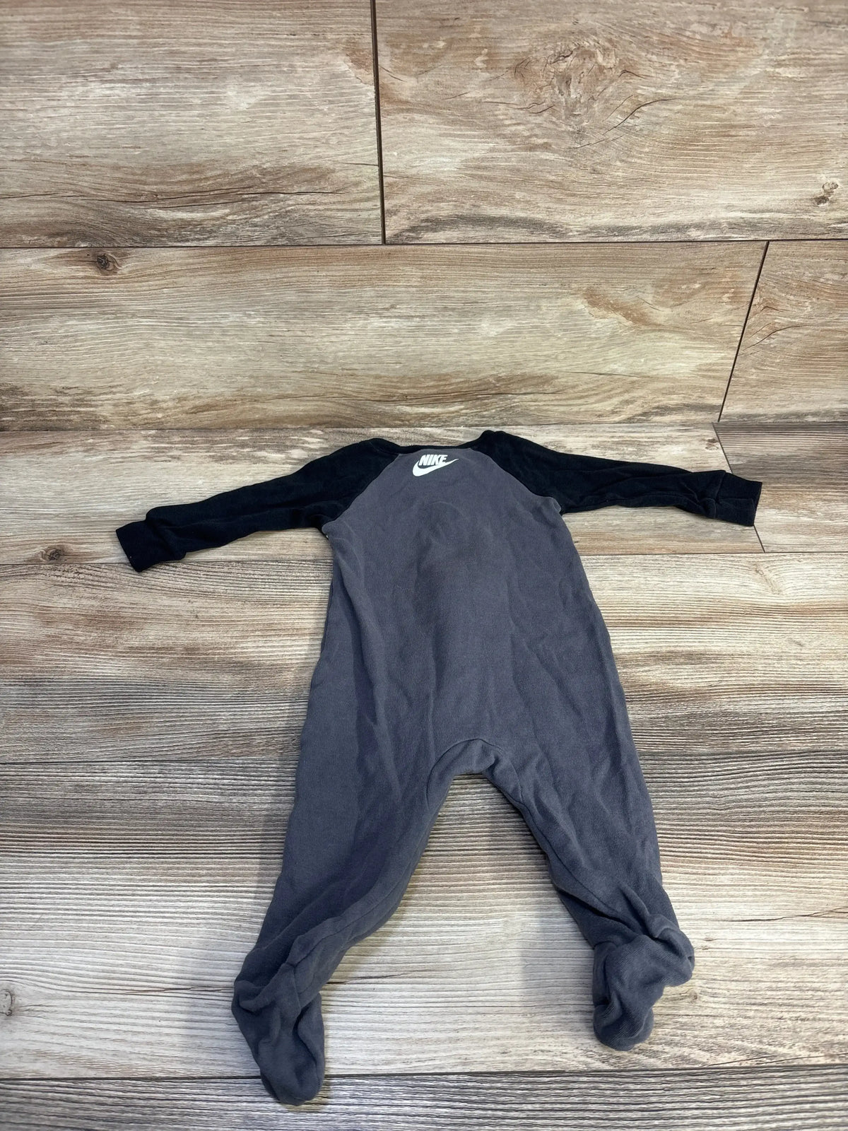 Front flat lay of baby footed sleeper with black raglan sleeves, charcoal body and white Nike logo on wood background
