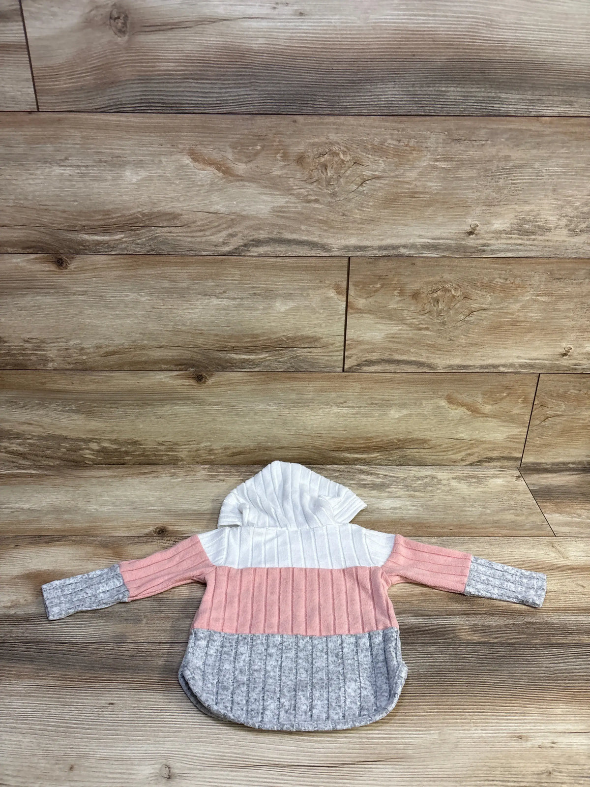 Back view of toddler hooded sweater showcasing white hood, pink midsection, and gray ribbed hem and cuffs on wood background