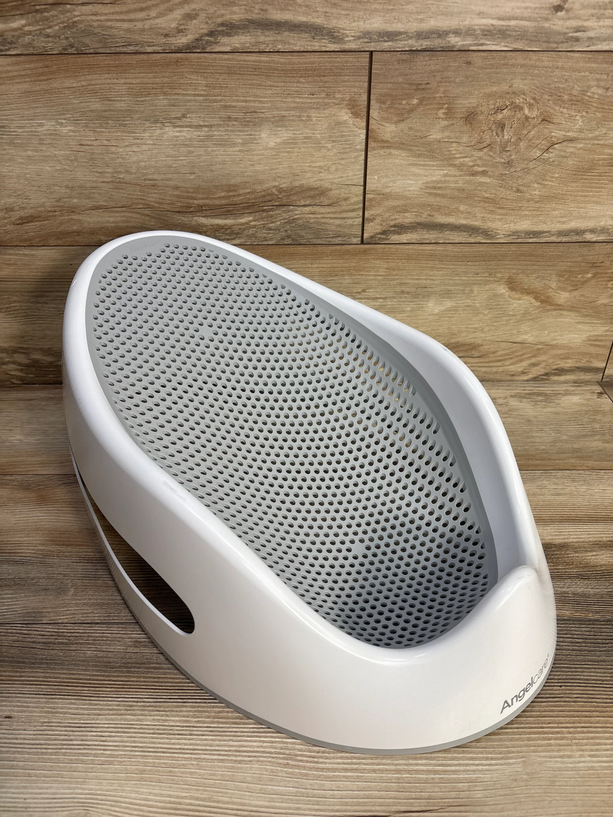 White perforated baby bath support on wood floor, Angelcare brand