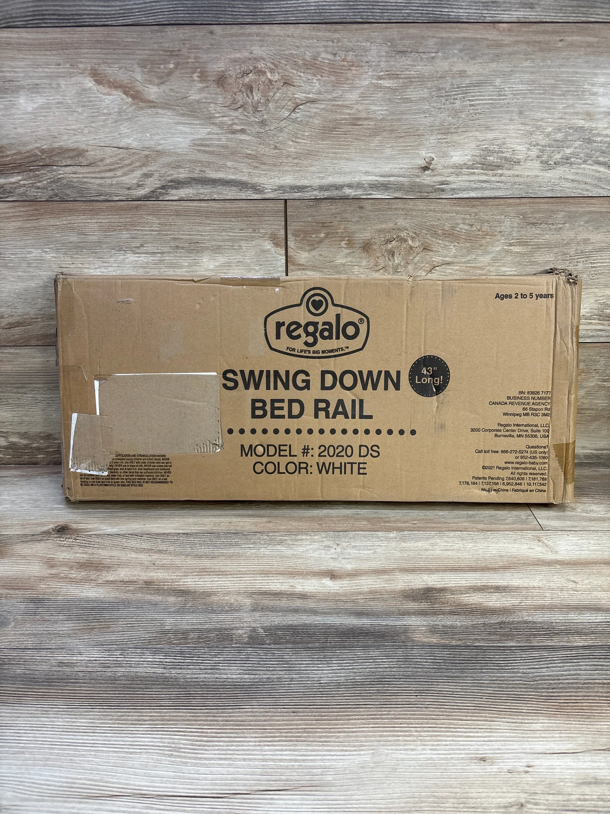 Front of boxed Regalo swing down bed rail showing large Swing Down Bed Rail label, 43 inch length and color white on wood-plank background
