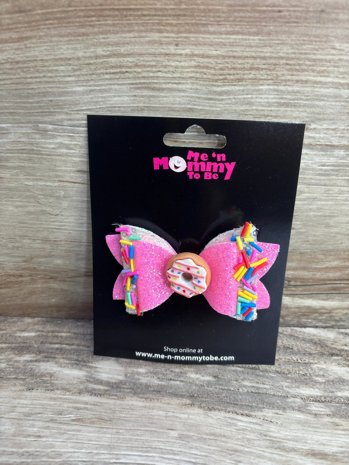 Front view of pink layered glitter donut hair bow with rainbow sprinkle trim and donut charm on black display card